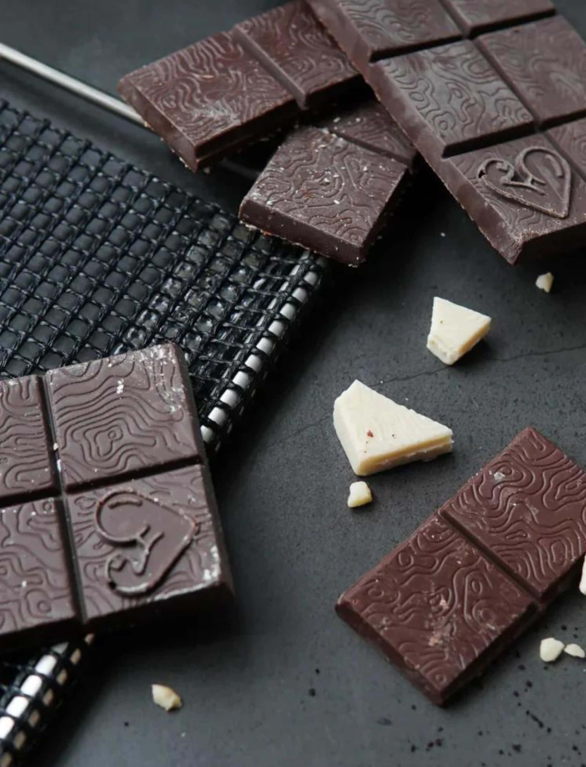 Dark Chocolate 桌布 壁紙 — 濃郁的黑巧克力和白巧克力條，帶有複雜的漩渦圖案，放在黑色網格和石板表面上。