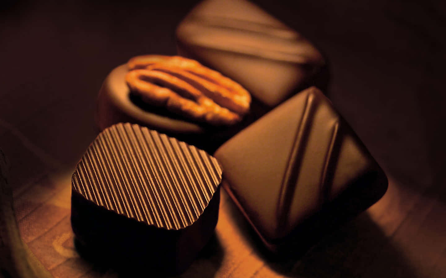 Brown Chocolate 桌布 壁紙 — 濃郁的黑巧克力搭配山核桃，表面紋理在柔和金色燈光下於木質表面上溫暖地閃耀。