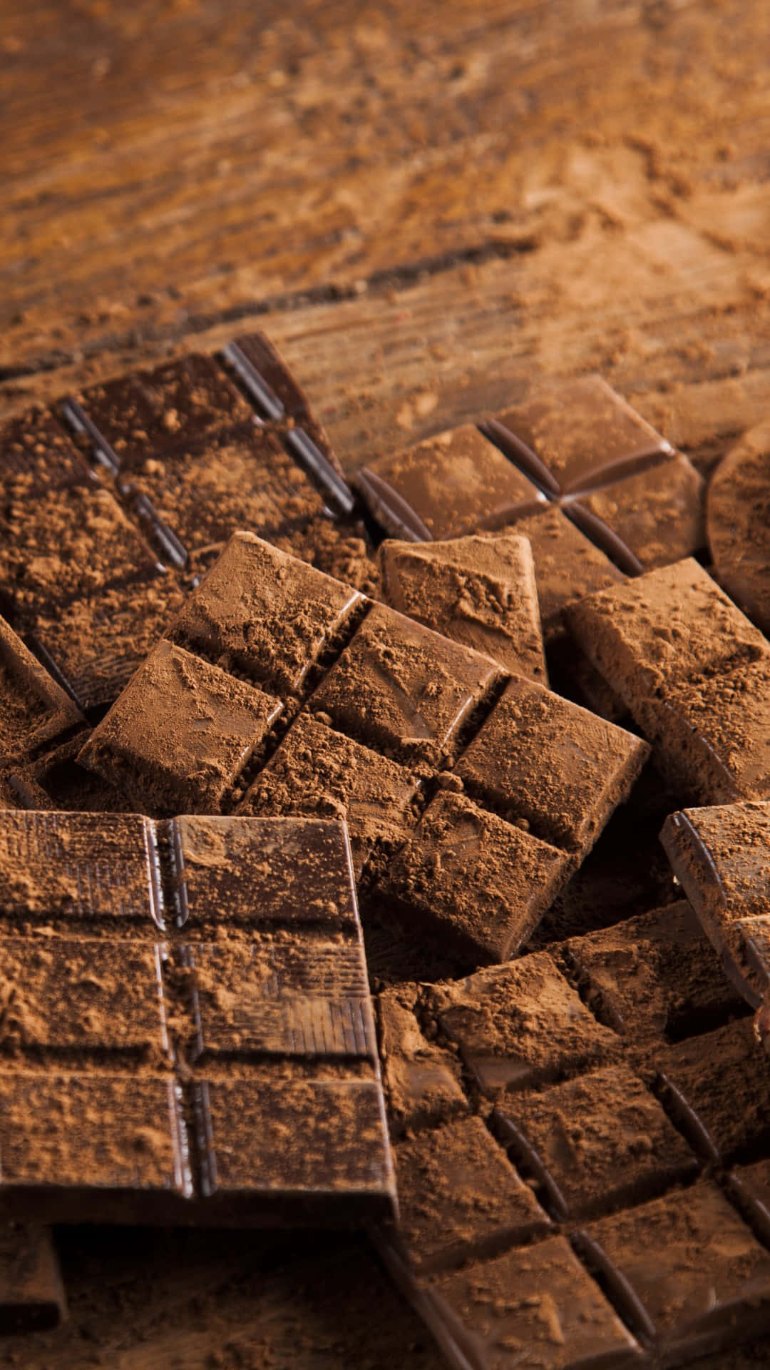 Chocolate 桌布 壁紙 — 濃郁的黑巧克力方塊撒上可可粉，放在質樸的木質表面上。