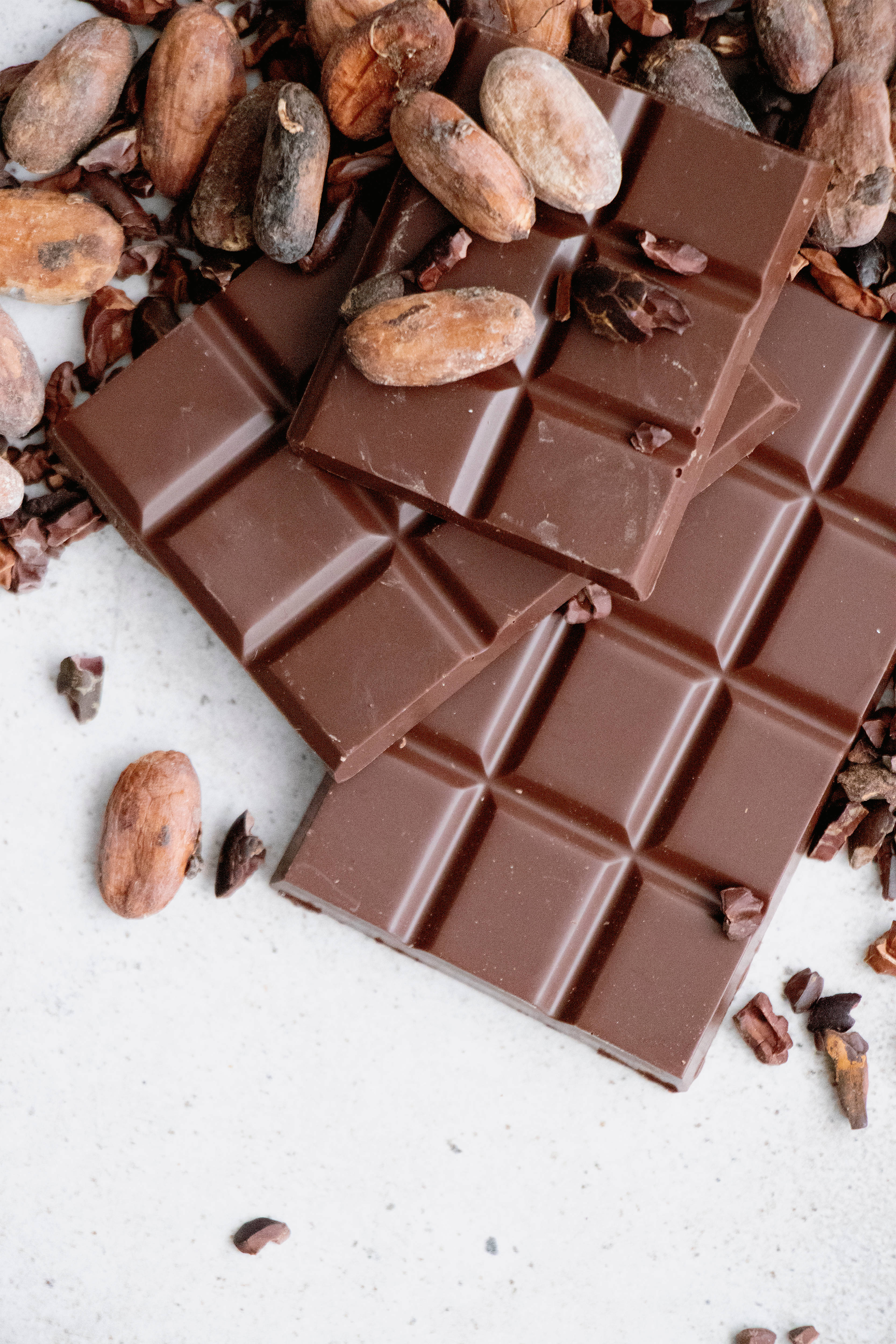 Chocolate 桌布 壁紙 — 濃郁的黑巧克力條，可可豆散落在淺色斑點表面上。