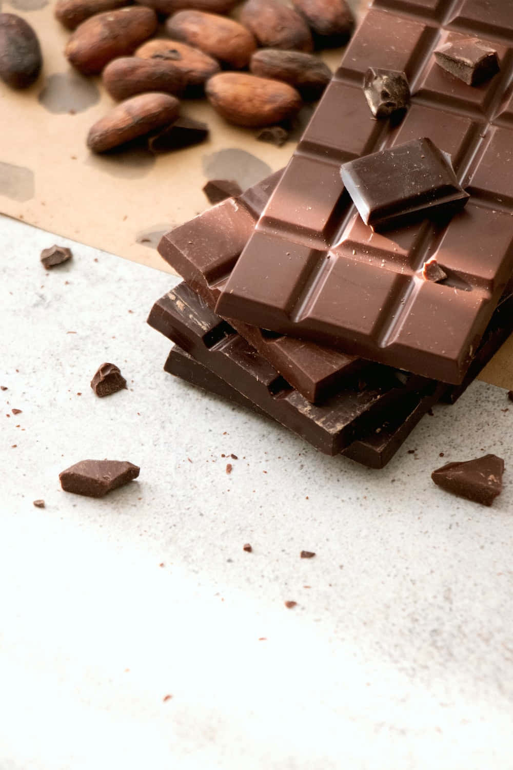 Dark Chocolate 桌布 壁紙 — 濃郁的黑巧克力條和可可豆放在有紋理的白色表面上，周圍散落著碎屑。