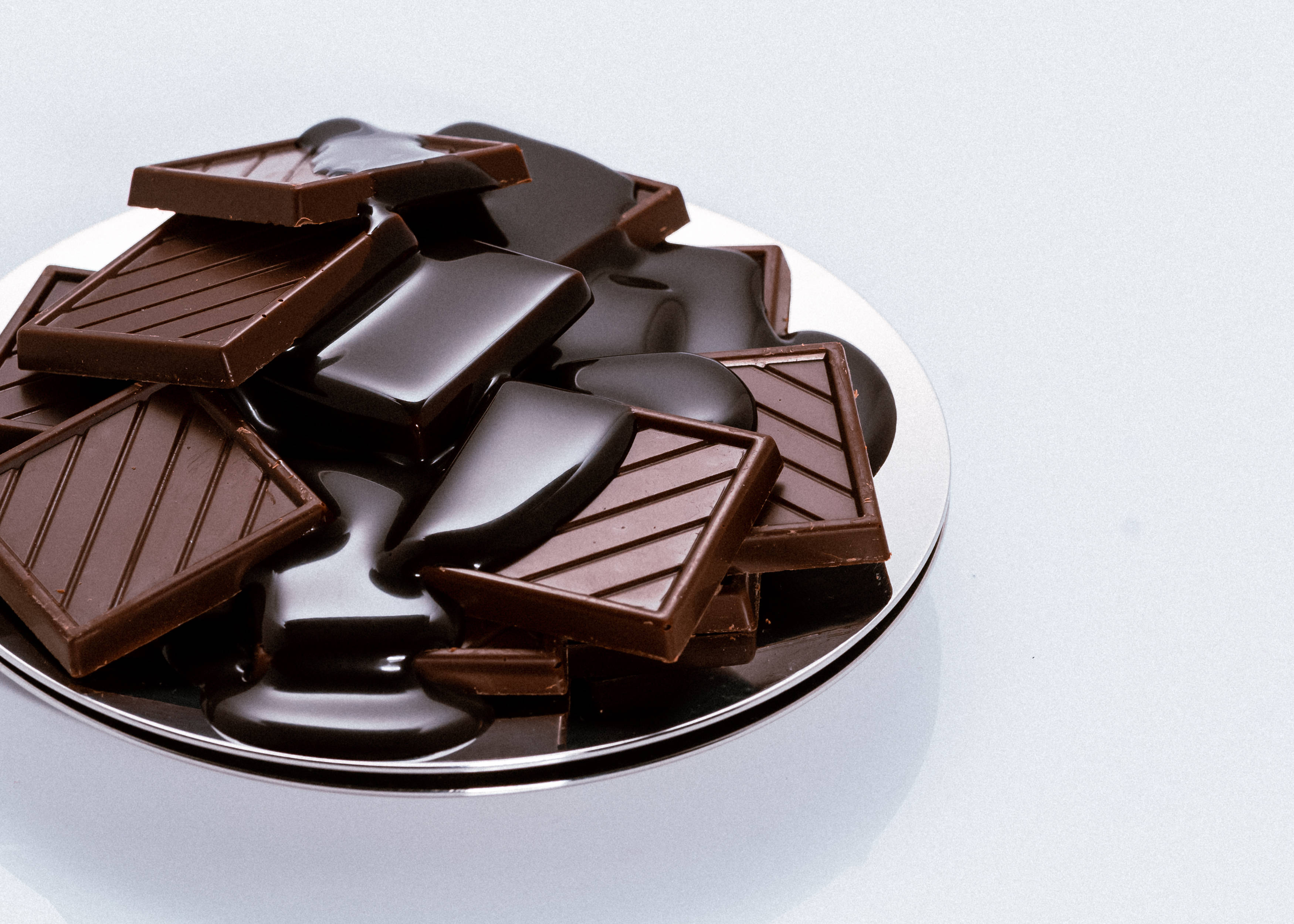 Chocolate 桌布 壁紙 — 濃郁的黑巧克力條和融化的巧克力池在銀色盤子上閃閃發光，背景是潔淨的白色。