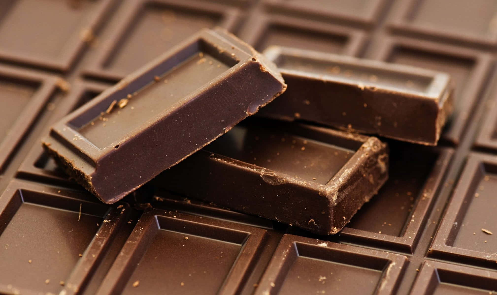 Brown Chocolate 桌布 壁紙 — 濃郁的黑巧克力棒被折成方塊，表面帶有光澤質感，並撒有可可粉。