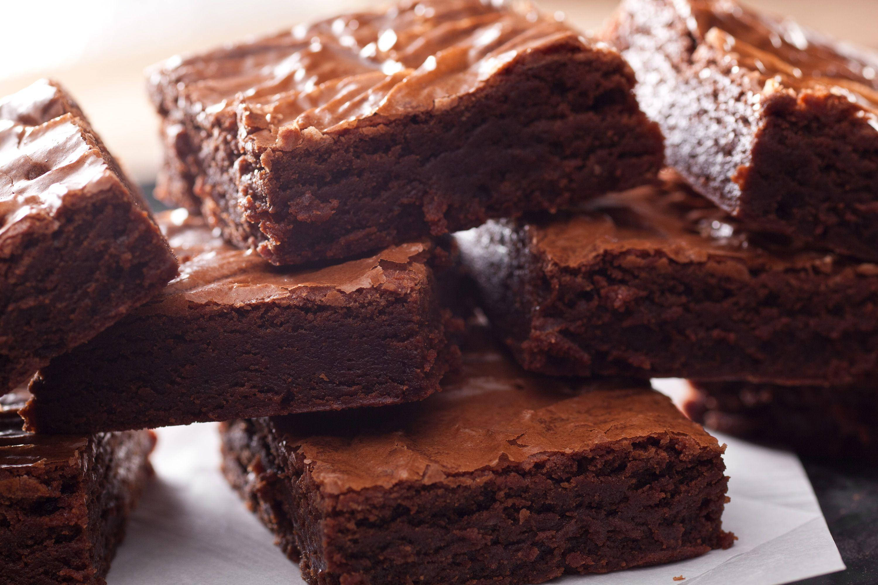 Brownies 桌布 壁紙 — 濃郁軟心巧克力布朗尼，配上閃亮巧克力糖霜，誘人地疊放在烘焙紙上。
