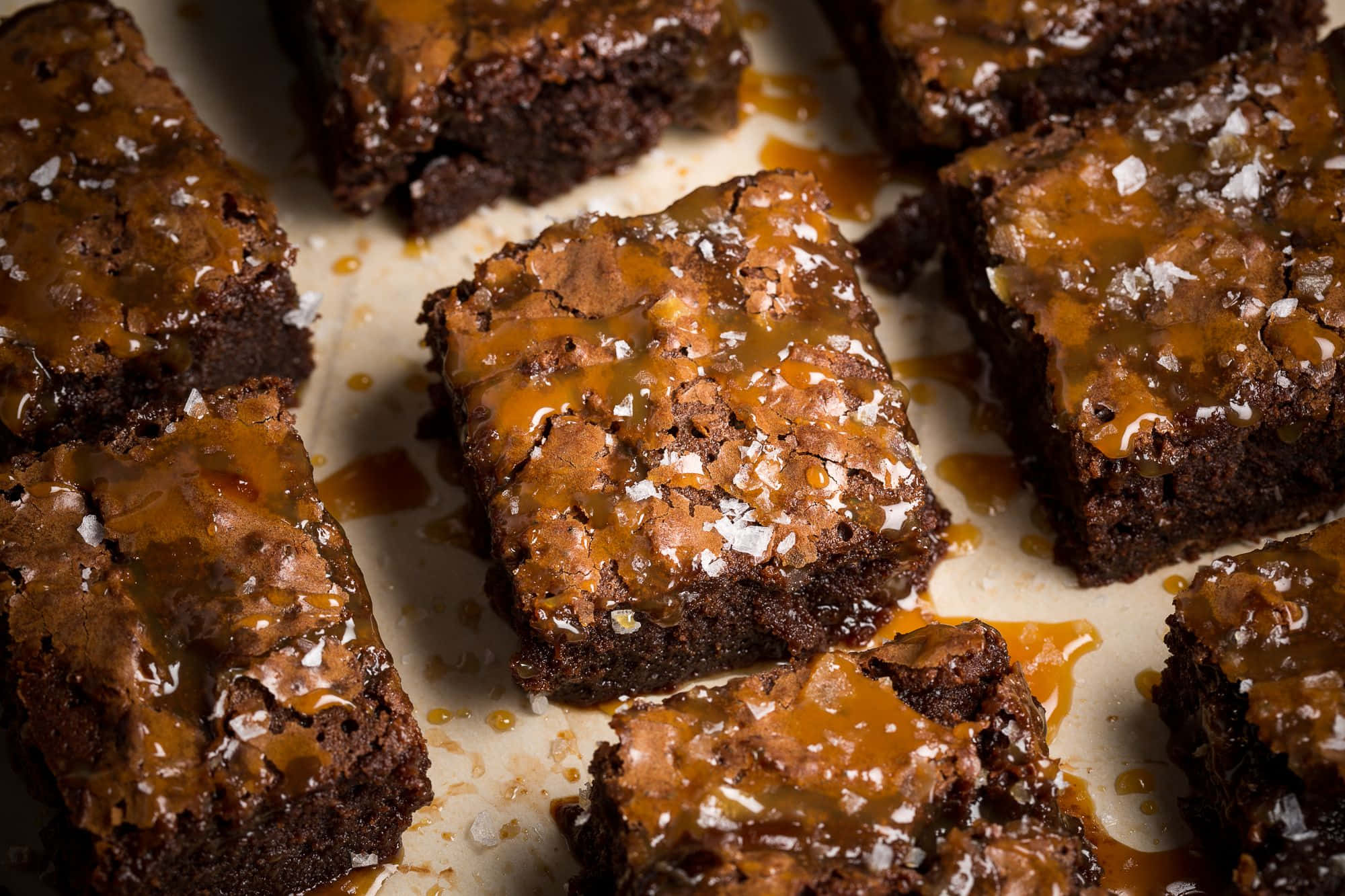 Caramel Brownie 桌布 壁紙 — 濃郁軟心布朗尼，上面鋪滿閃亮焦糖和片狀海鹽，放在烘焙紙上。