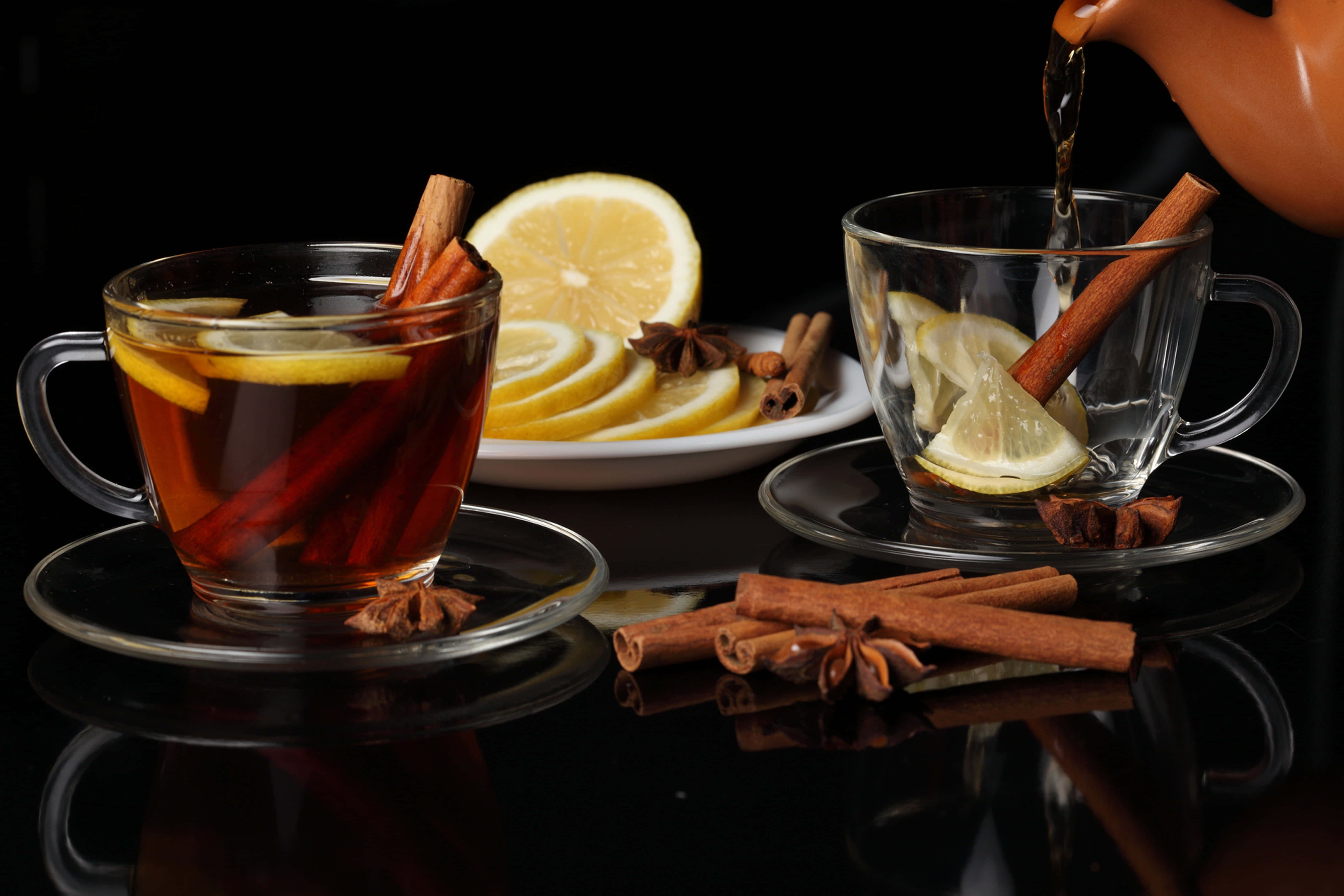 Mulled Wine 桌布 壁紙 — 濃郁香料茶加入檸檬和肉桂，從陶壺倒入玻璃杯，置於亮面黑色桌上。