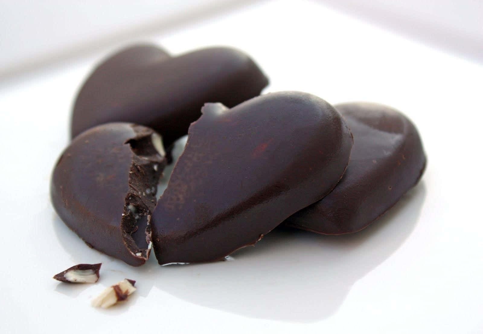 Chocolate 桌布 壁紙 — 濃郁黑巧克力心形糖果，內含杏仁餡料，放在白色盤子上，其中一塊破開露出果仁內餡。
