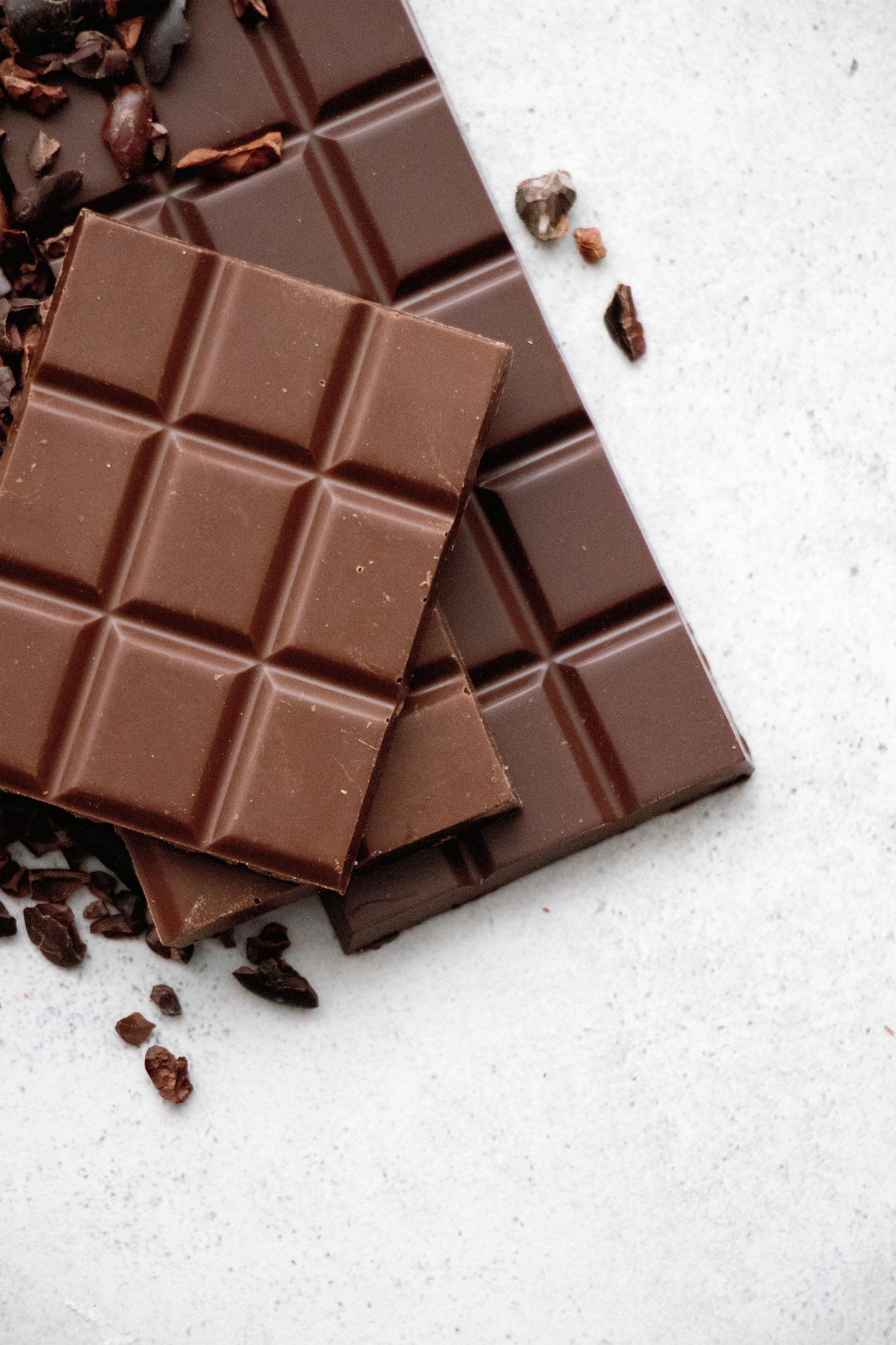 Chocolate 桌布 壁紙 — 濃郁黑巧克力條，上面散落可可碎粒，置於潔白有紋理的表面上。