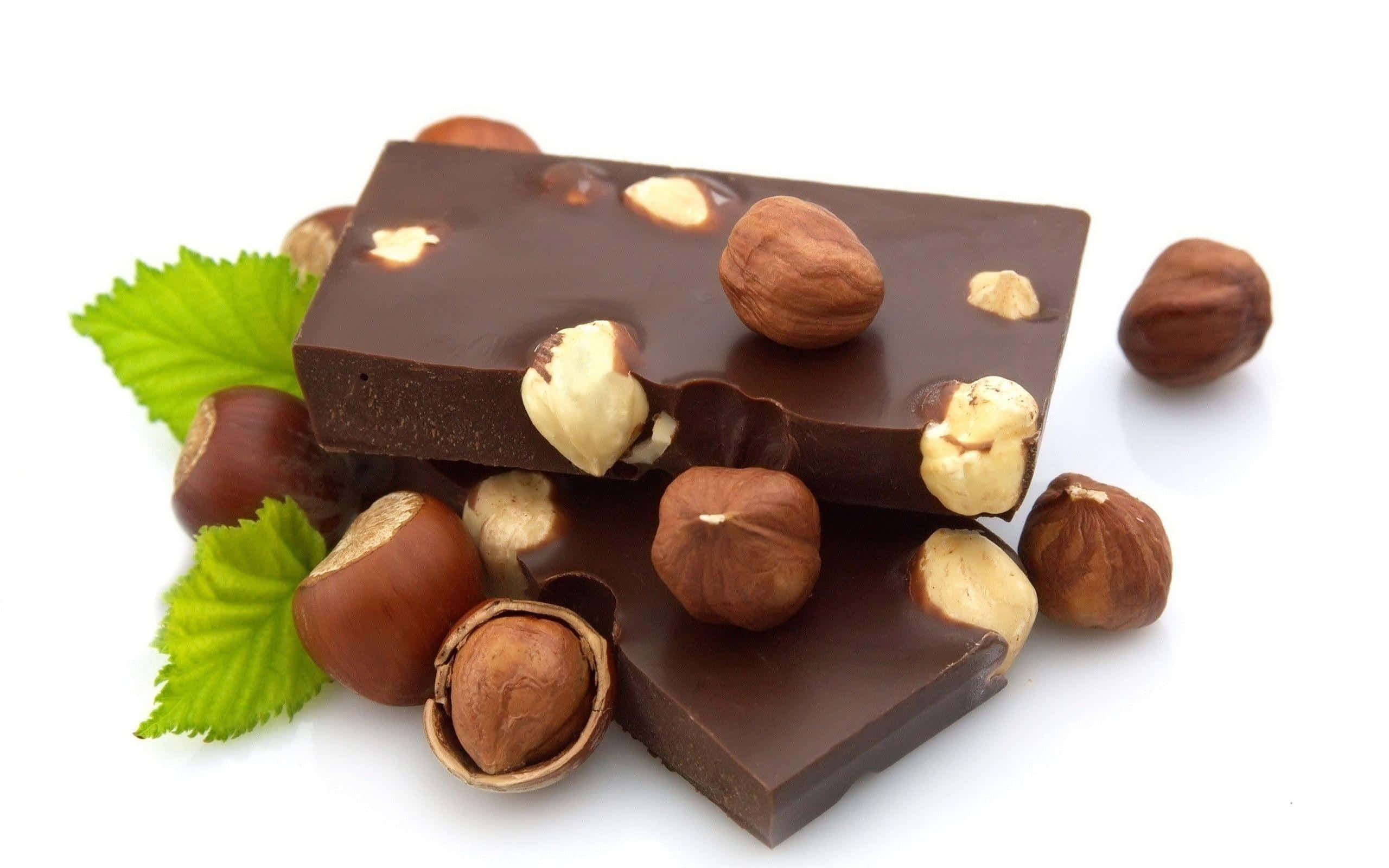 Brown Chocolate 桌布 壁紙 — 濃郁黑巧克力條，綴以完整及碎裂的榛子和新鮮綠葉，置於白色背景上。