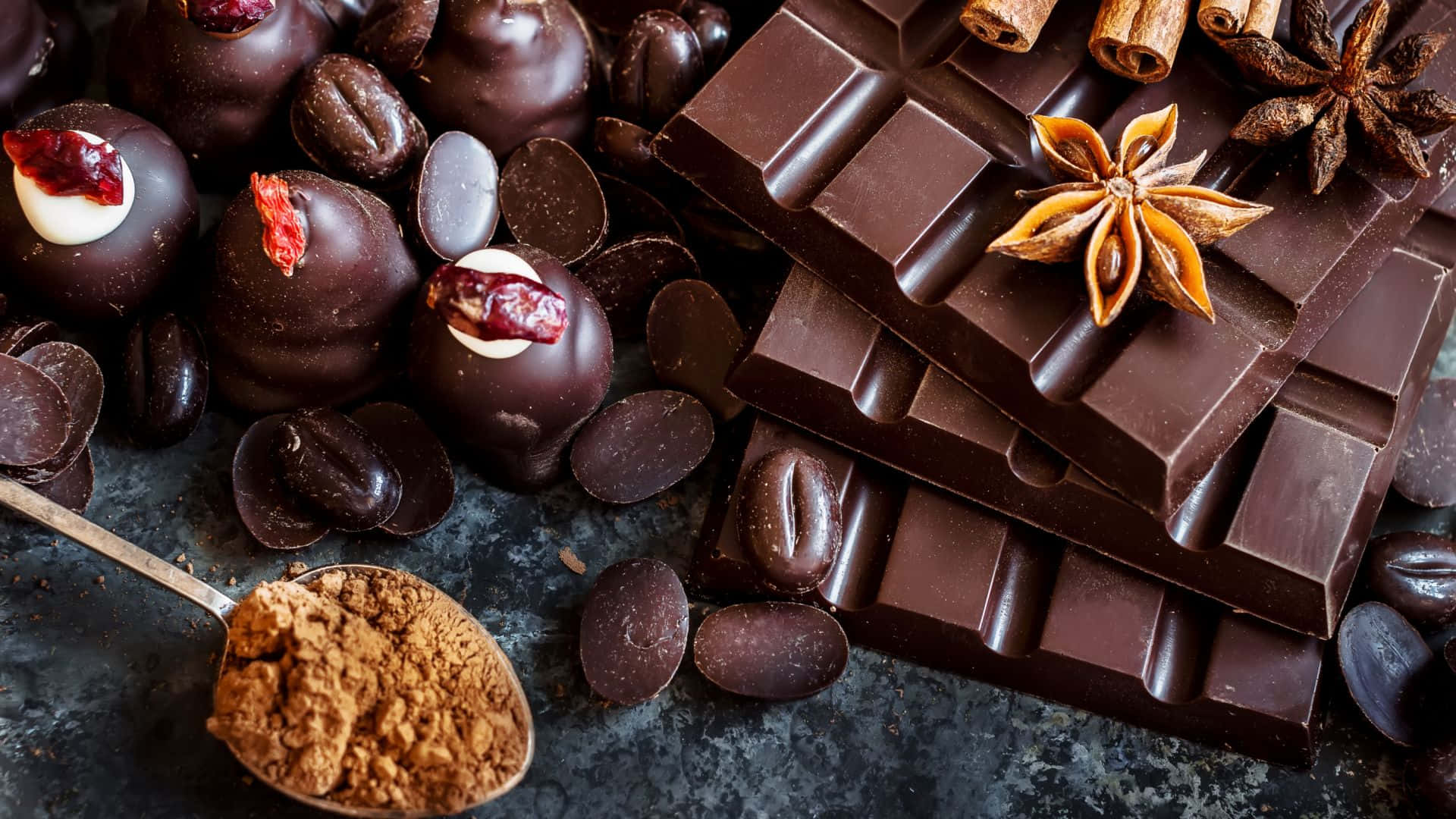 Chocolate 桌布 壁紙 — 濃郁黑巧克力條和松露巧克力配八角茴香和可可粉，置於深色紋理表面上。