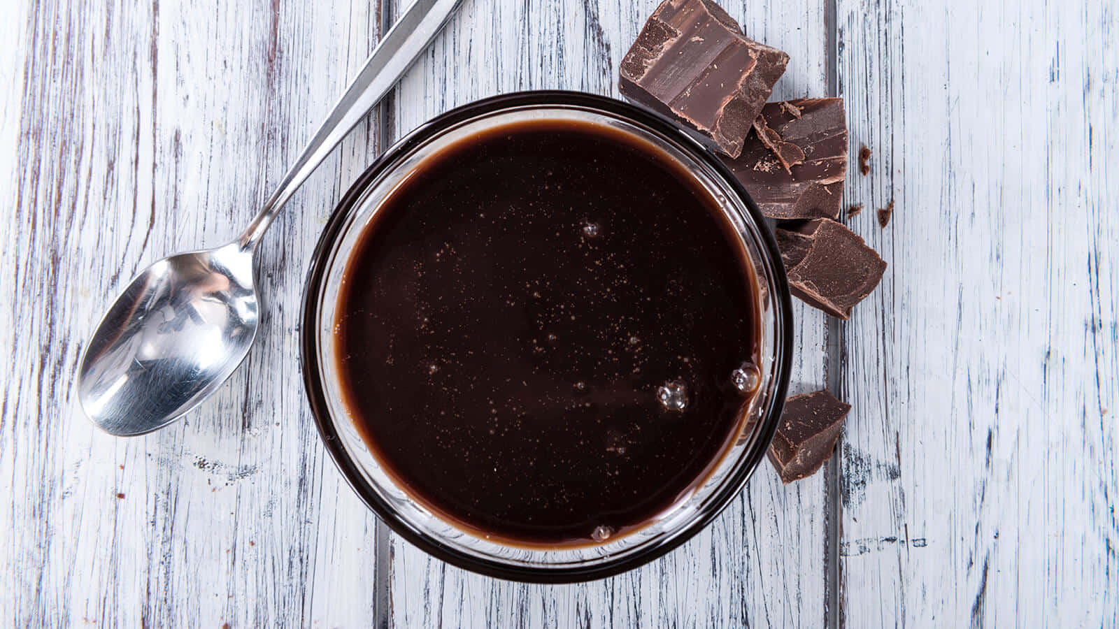 Dark Chocolate 桌布 壁紙 — 濃郁黑巧克力醬放在玻璃碗中，配上碎巧克力塊和湯匙，置於風化白色木面上。