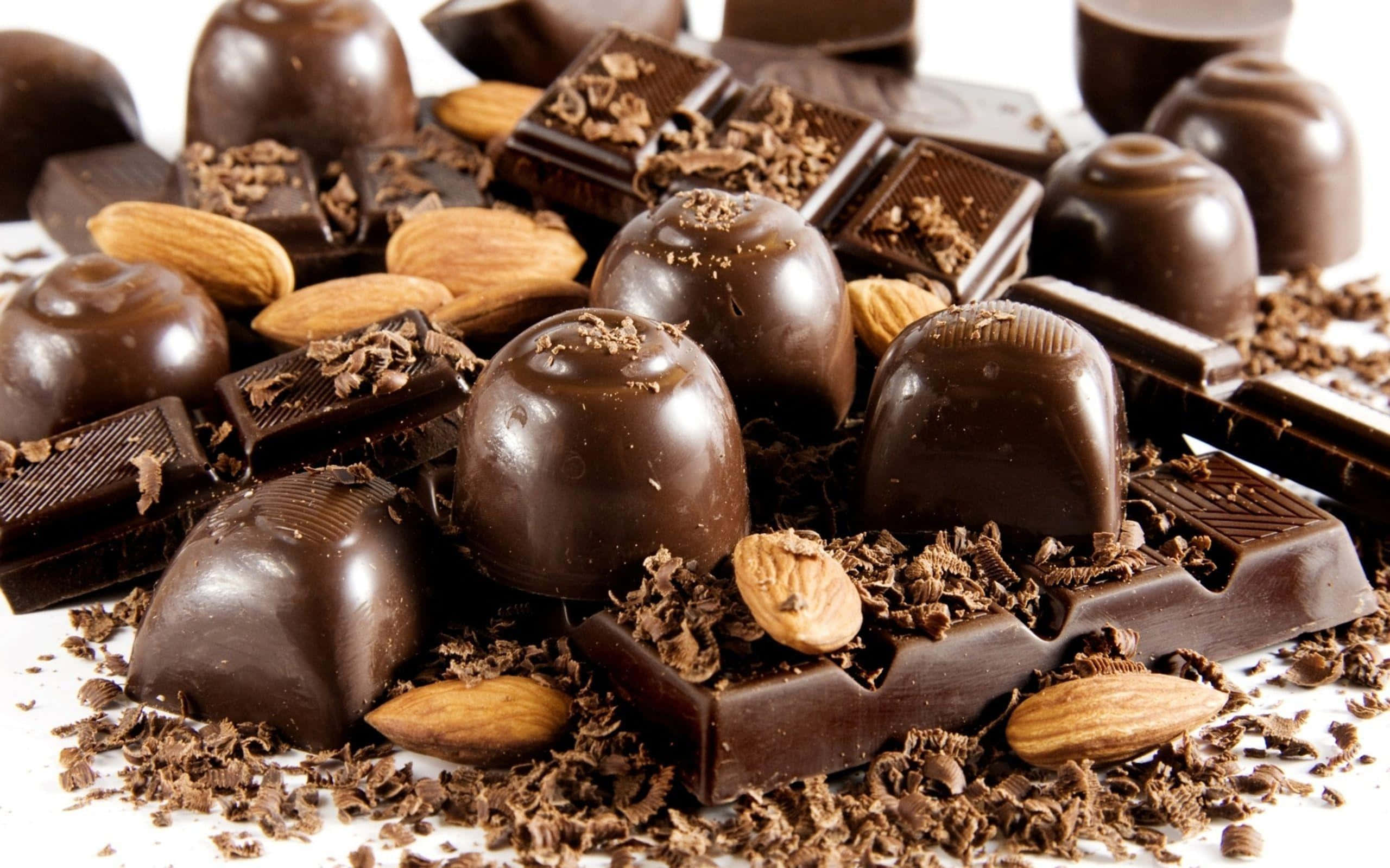 Brown Chocolate 桌布 壁紙 — 濃郁黑松露巧克力和巧克力條，配以整粒杏仁和可可碎屑，散落在白色表面上。