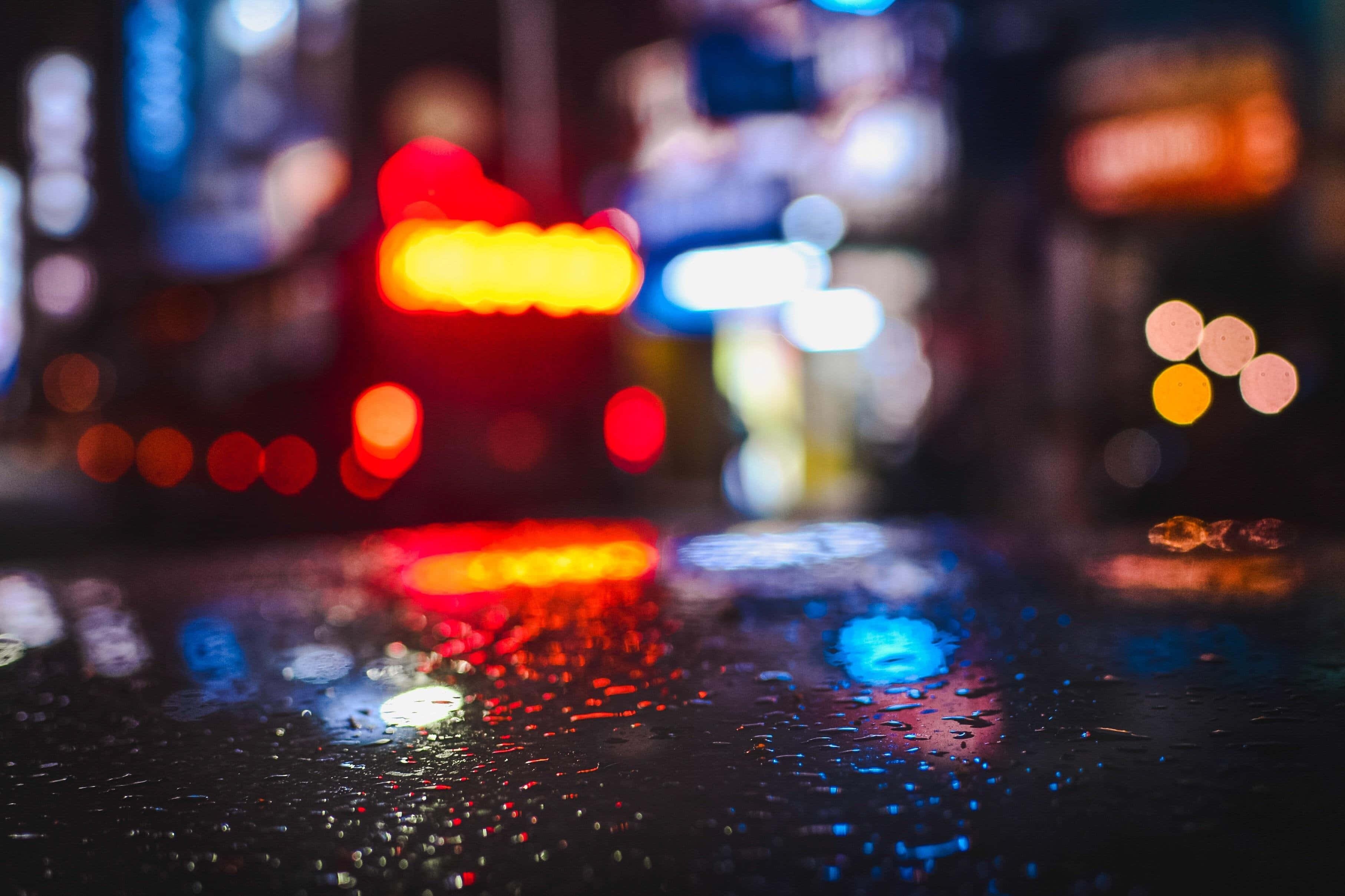Rainy Day 桌布 壁紙 — 濕漉漉的人行道上，雨滴反射著繁華都市夜晚模糊的霓虹燈光。