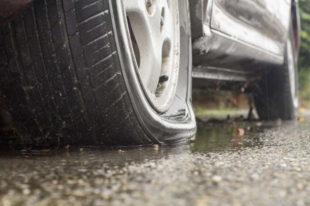 Flat Tire 桌布 壁紙 — 濕漉漉的路面上，一個扁掉的車胎，周圍有泥巴和水花濺起的特寫。
