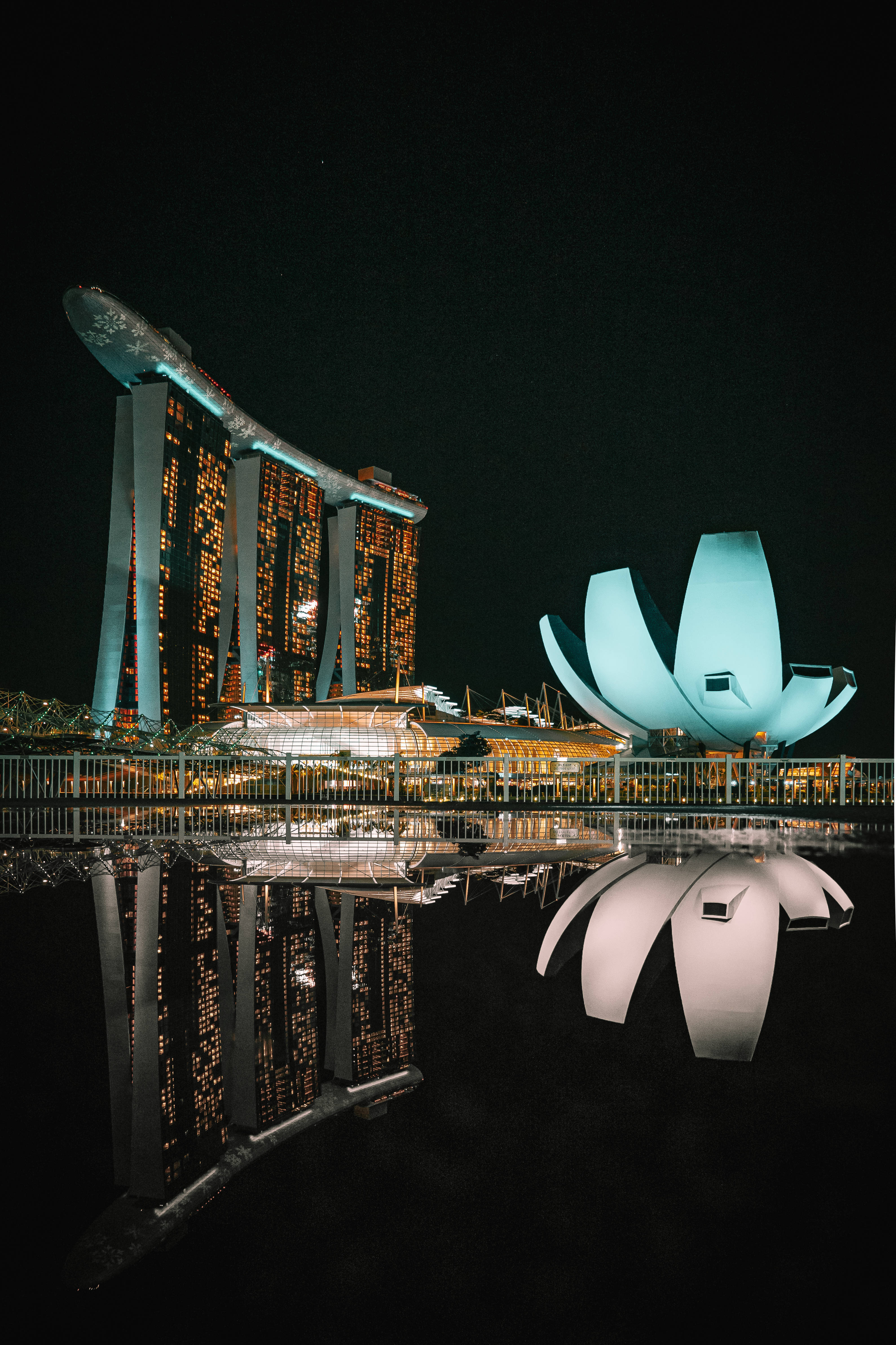 iPhone 桌布 壁紙 — 濱海灣金沙和藝術科學博物館在夜晚發光，在黑暗的天空下於水中完美倒映。