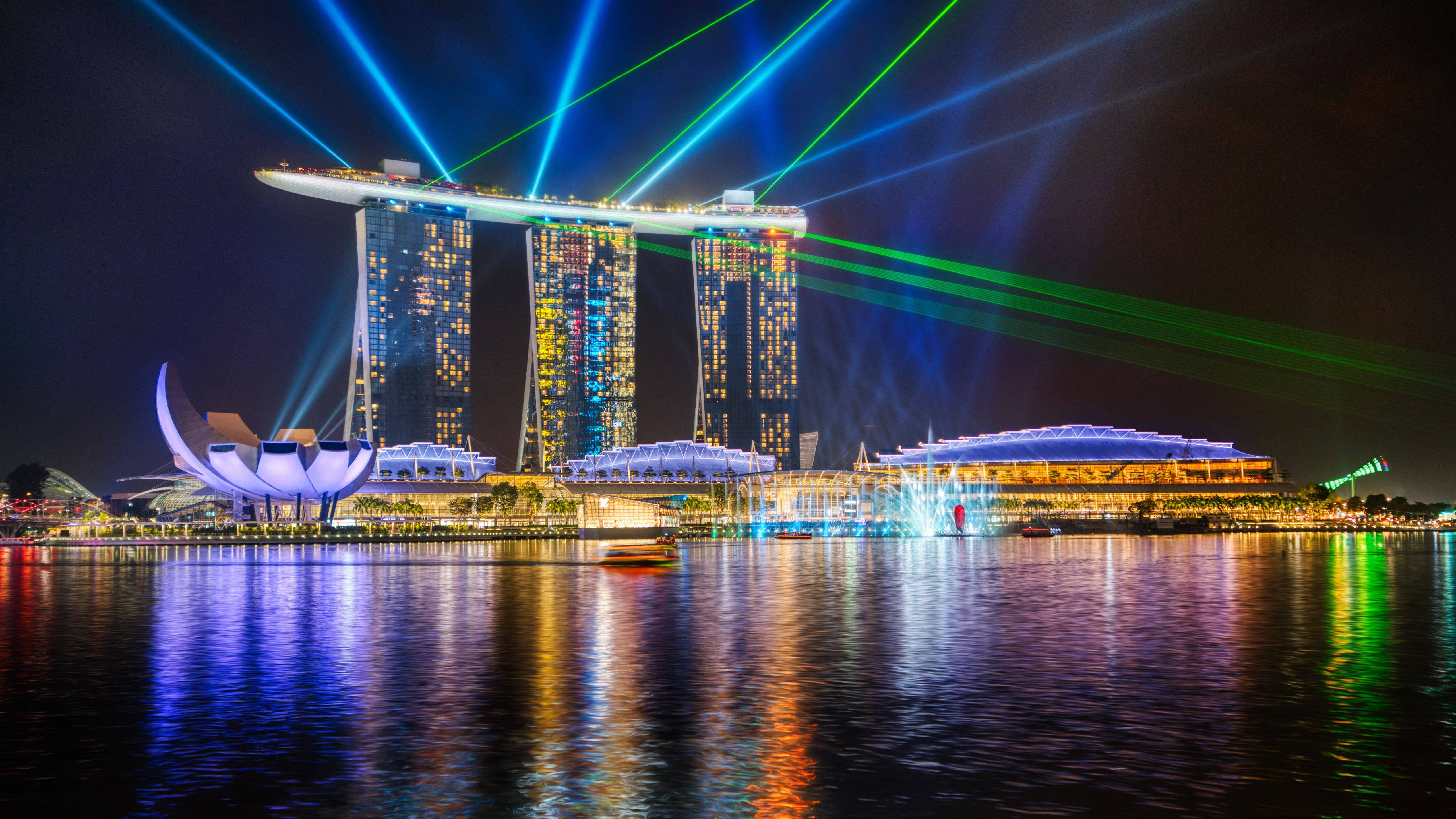 Singapore 桌布 壁紙 — 濱海灣金沙在夜間聳立於水面上，耀眼的藍色和綠色雷射光束照亮天空，並在平靜的水面上反射。