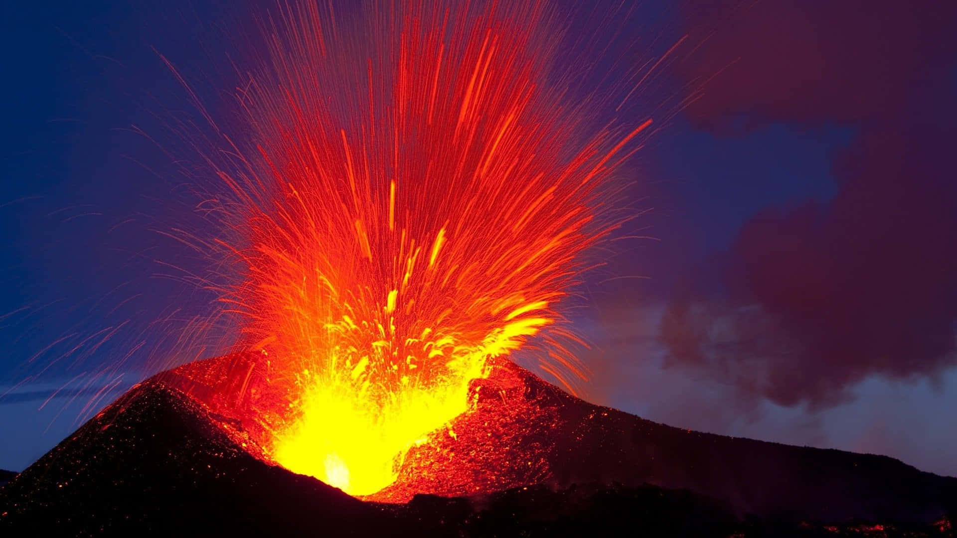 Volcano 桌布 壁紙 — 火山在夜間劇烈噴發，熾熱的橙色熔岩高高射入深紫色的天空。