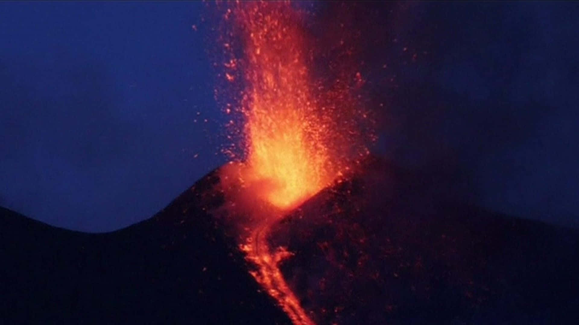 Flame 桌布 壁紙 — 火山在夜間猛烈爆發，明亮的橙色熔岩和發光的灰燼在深藍色天空中爆炸。