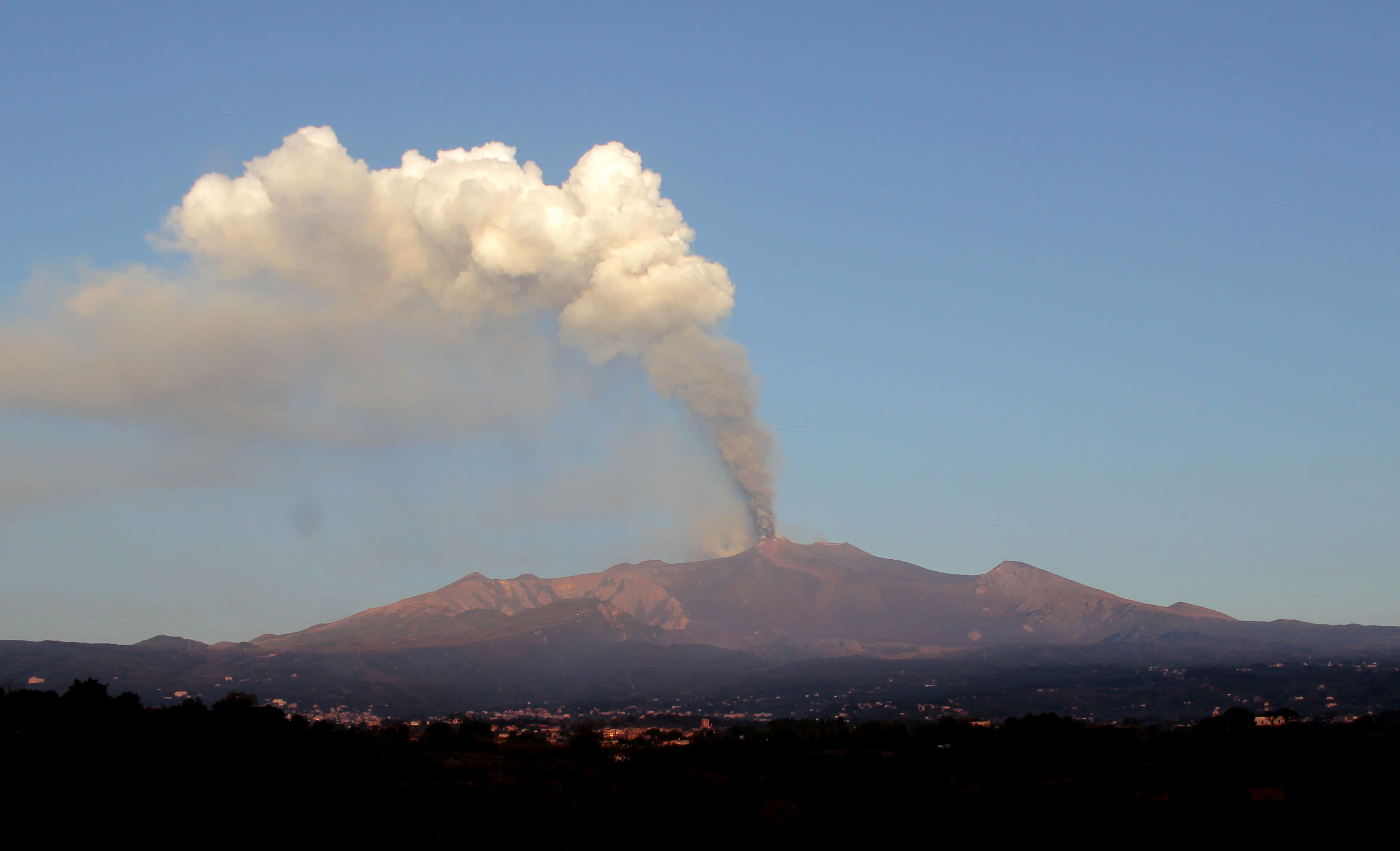 山景 桌布 壁紙 — 火山爆發，向遠方城鎮上空晴朗的藍天噴出大量火山灰和煙霧。