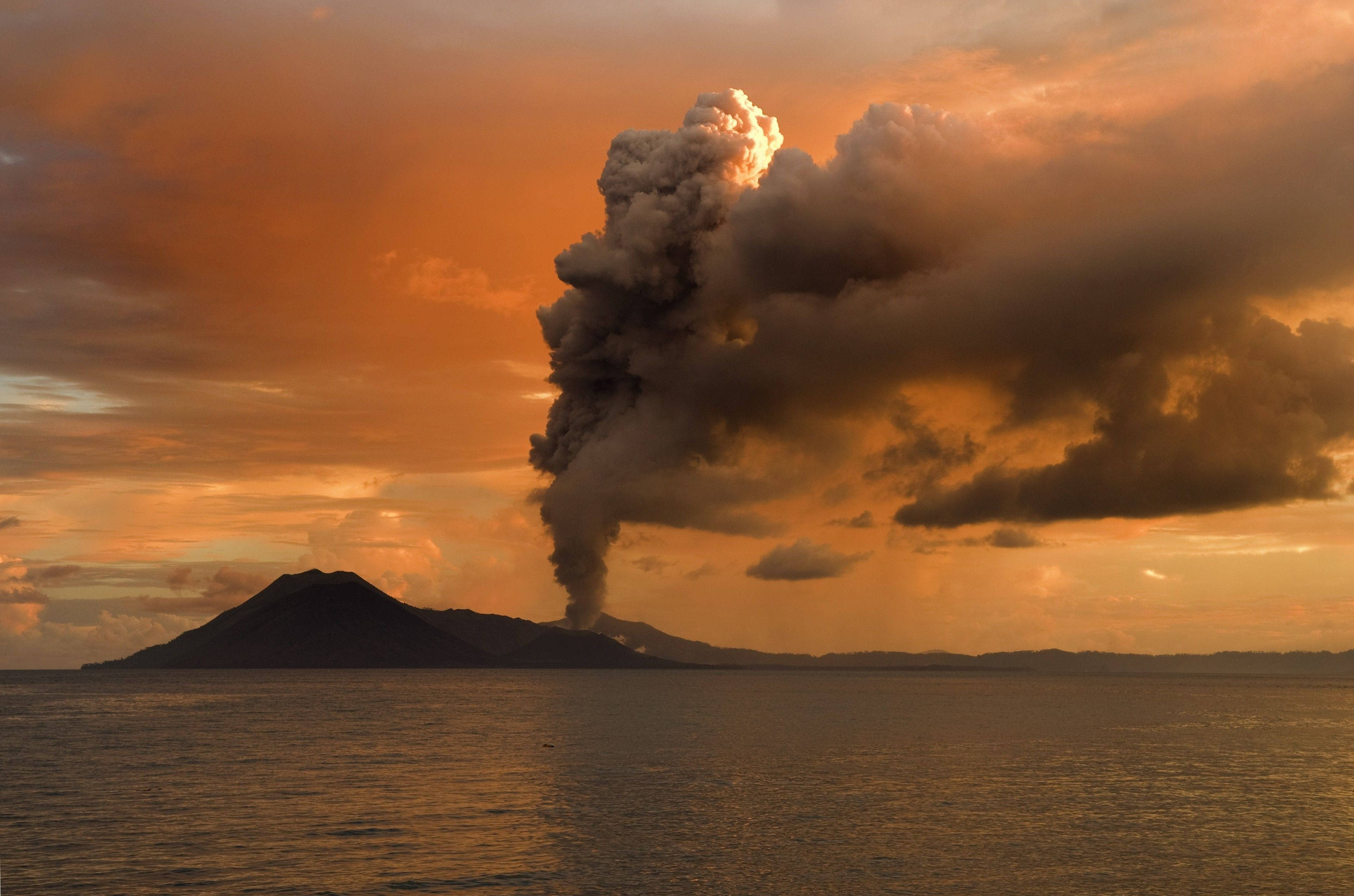 New 桌布 壁紙 — 火山爆發將巨大的火山灰雲噴向平靜海洋上方火紅的橙色日落天空。