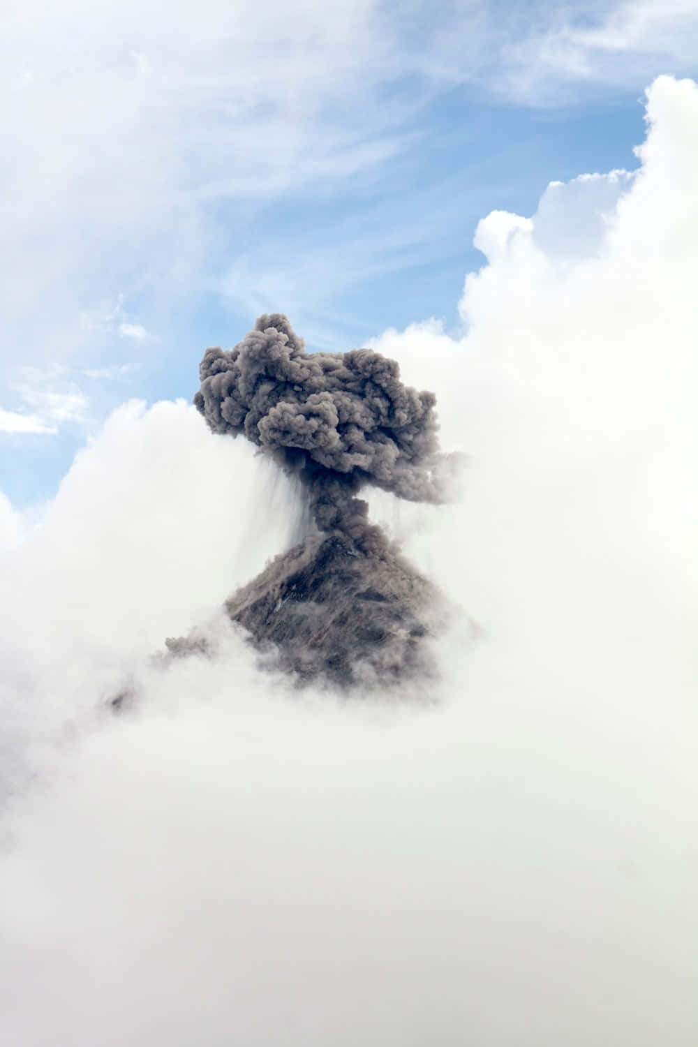 Volcano 桌布 壁紙 — 火山爆發將深色火山灰噴向被 fluffy 白色雲朵環繞的明亮藍天高空。