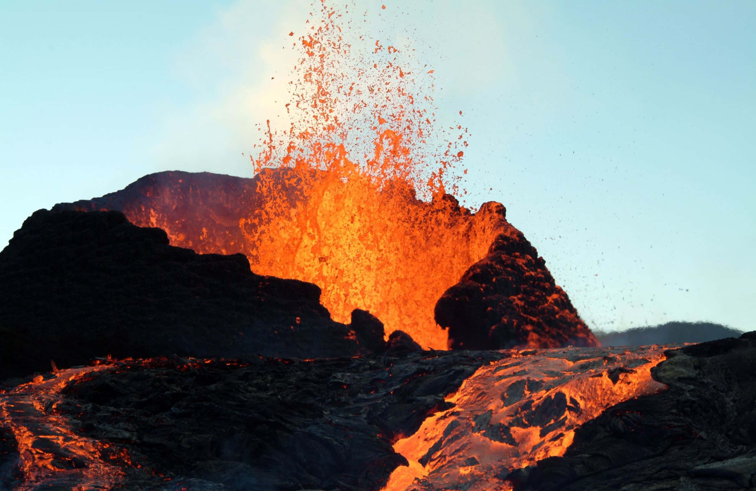 2560x1664 桌布 壁紙 — 火山爆發將熾熱的橙色熔岩和發光的碎片噴射到黃昏時分清澈的藍天中。