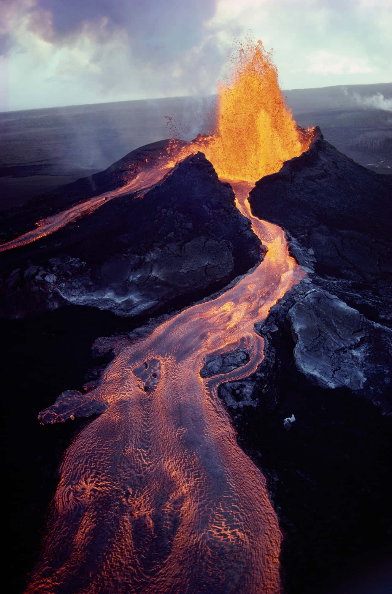 Volcano 桌布 壁紙 — 火山爆發將熾熱的熔岩噴向天空，發光的河流沿著崎嶇的黑色山坡奔流而下。