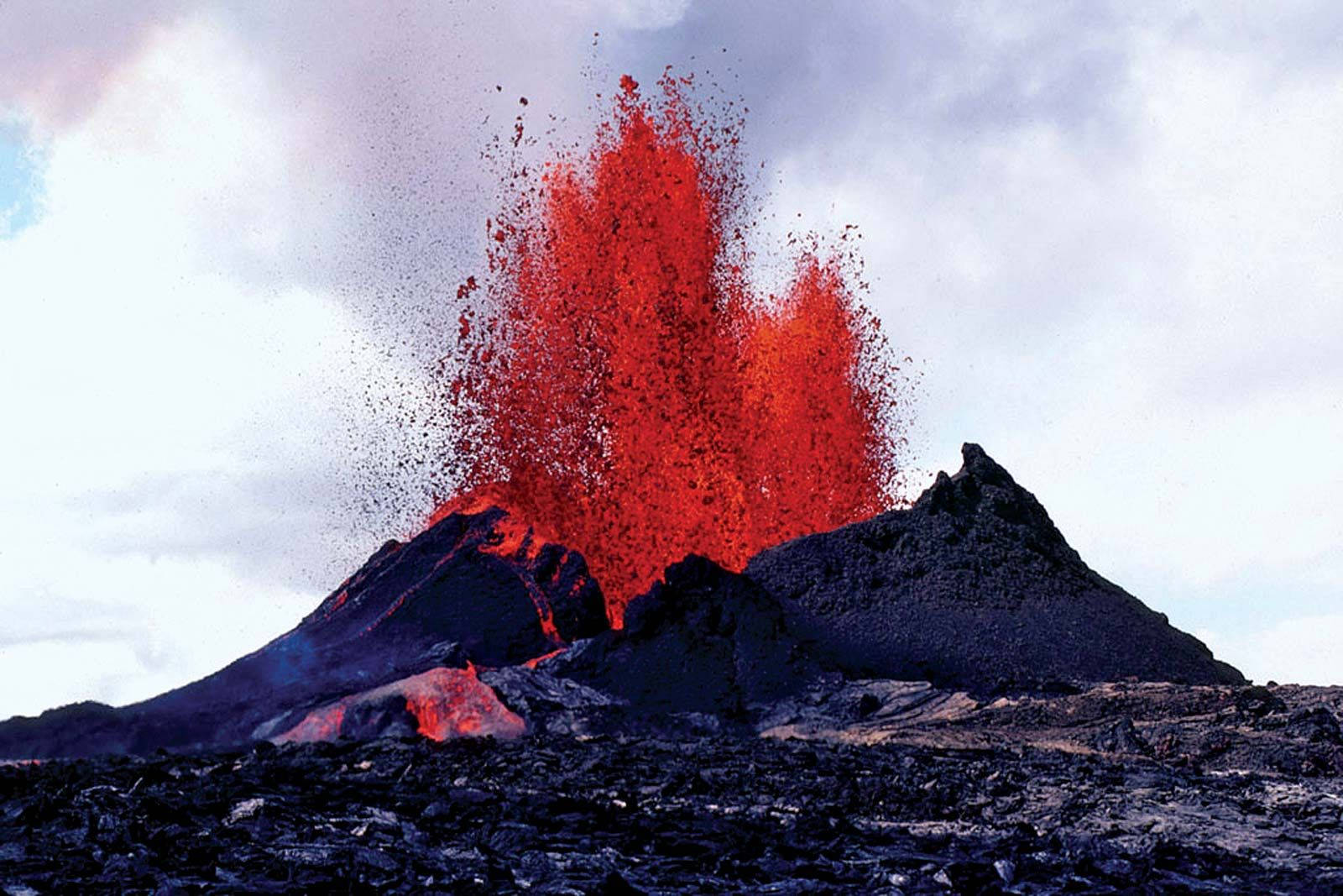 Volcano 桌布 壁紙 — 火山爆發將熾熱的紅色熔岩噴射到多雲的天空，下方是崎嶇的黑色地貌。