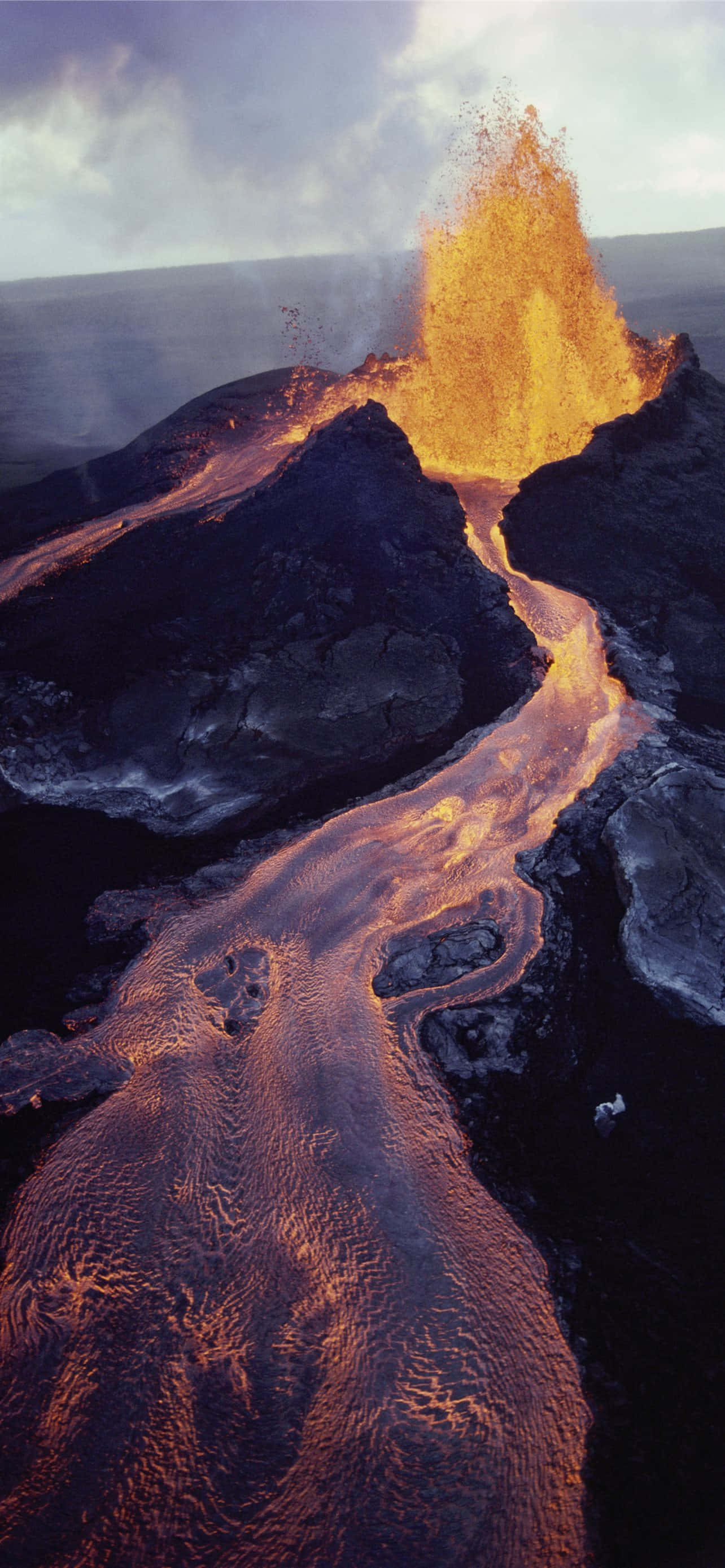 Volcano 桌布 壁紙 — 火山爆發的鳥瞰圖，熾熱的橙色熔岩沿著崎嶇的黑色岩石流入海洋。
