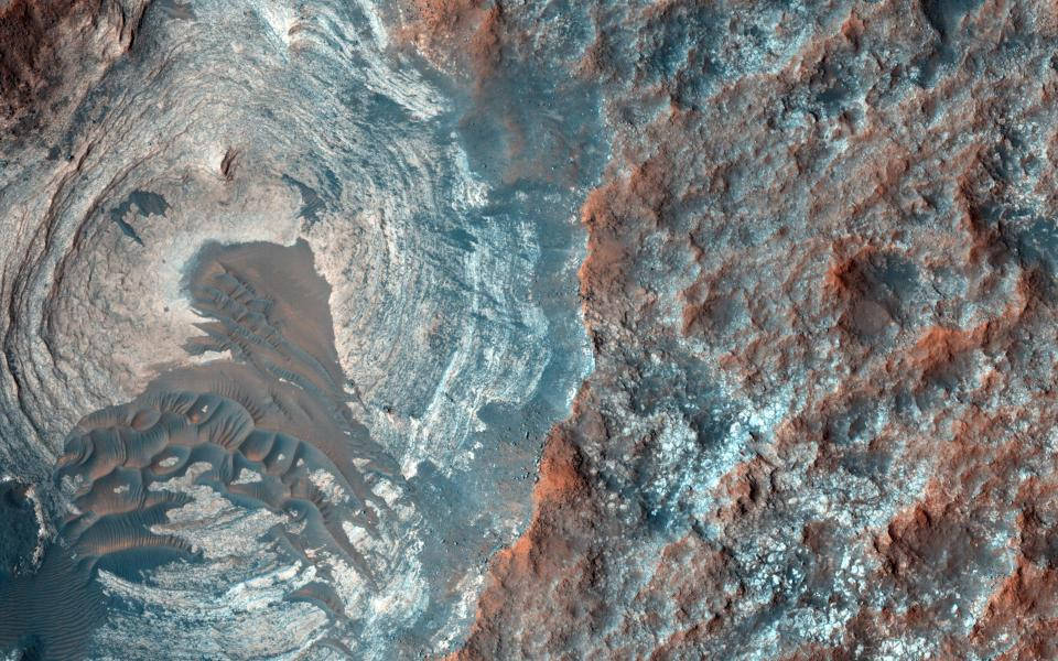 Nasa Aesthetic 桌布 壁紙 — 火星的鳥瞰圖，展示崎嶇的地形，帶有旋轉的灰塵圖案和鏽紅色和冰藍色調的層狀岩層。