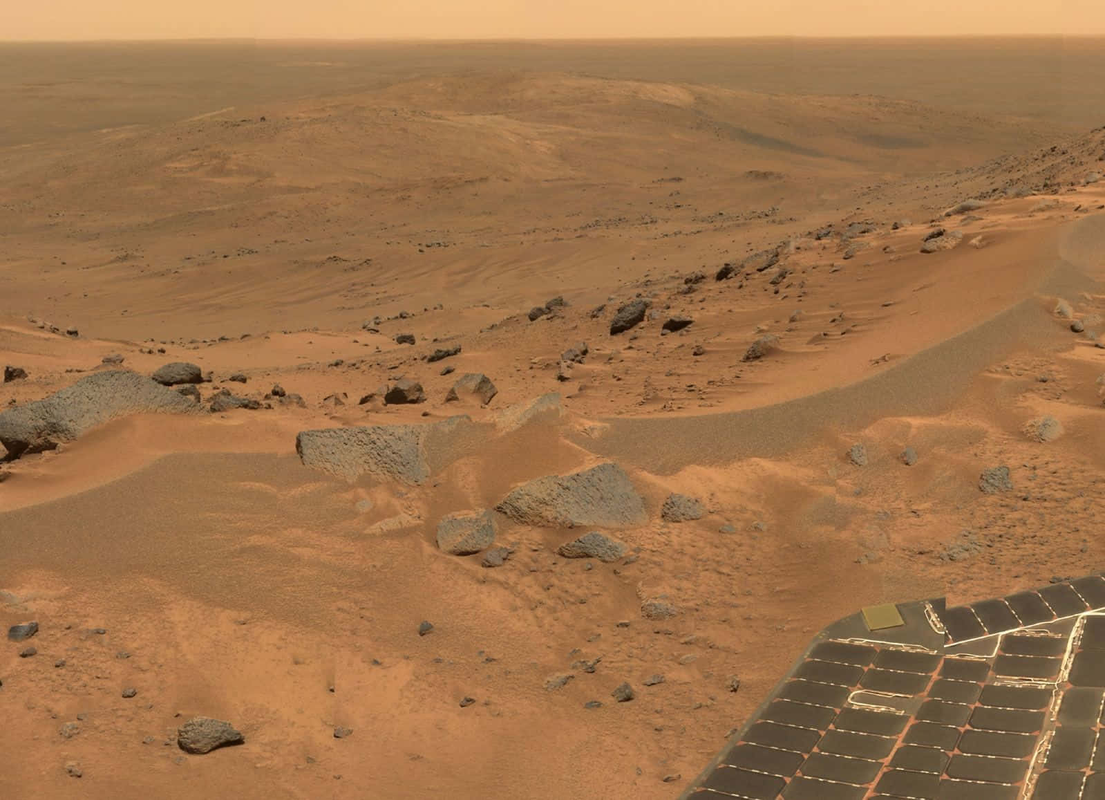Mars Landscape 桌布 壁紙 — 火星表面的航拍圖，前景是岩石地形和太陽能板，天空是朦朧的橙色。