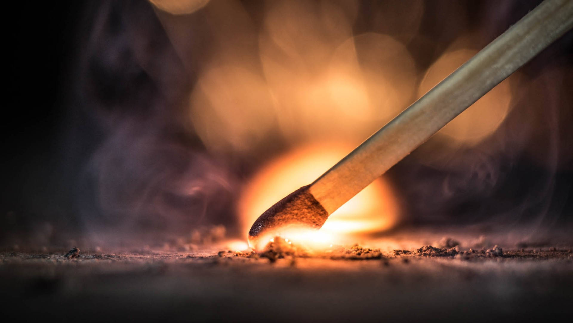 火焰動畫 桌布 壁紙 — 火柴點燃的特寫，帶有明亮的橙色火焰和縷縷煙霧，背景為模糊的深色。