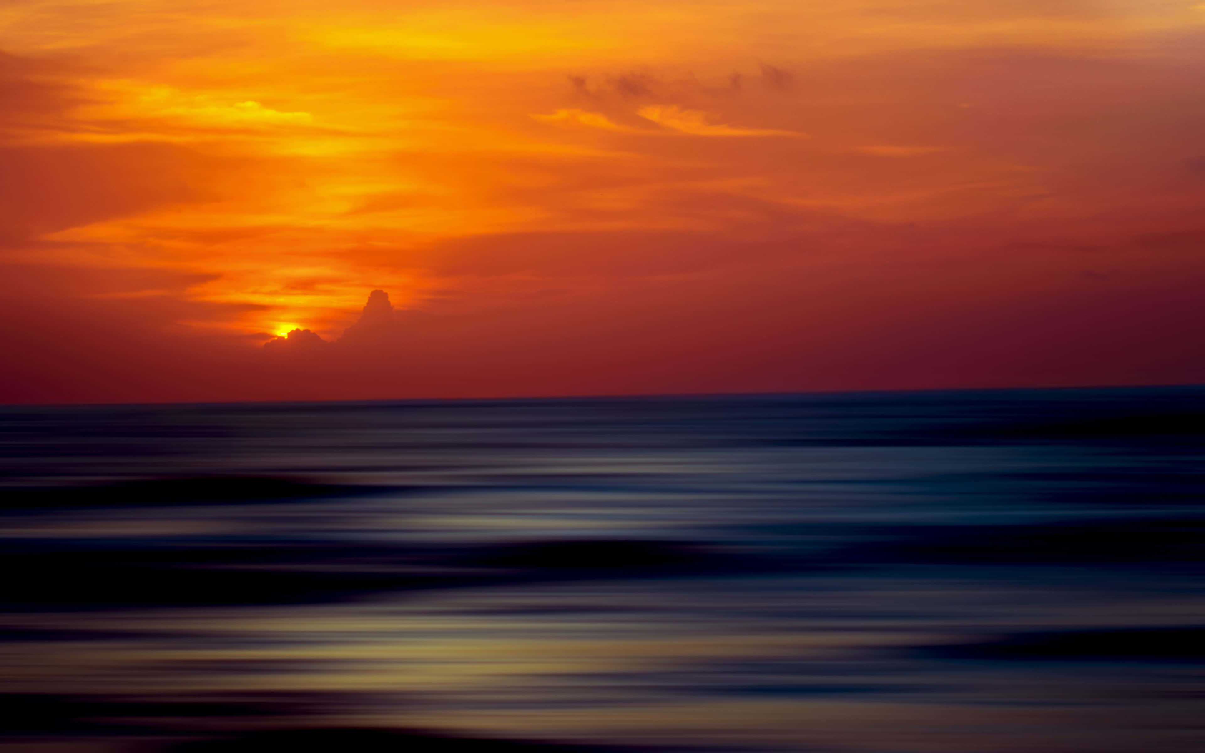 Sunset Ocean 桌布 壁紙 — 火熱的橙色日落照耀在動態模糊的海洋上，深藍色的波浪反射著天空溫暖的色調。