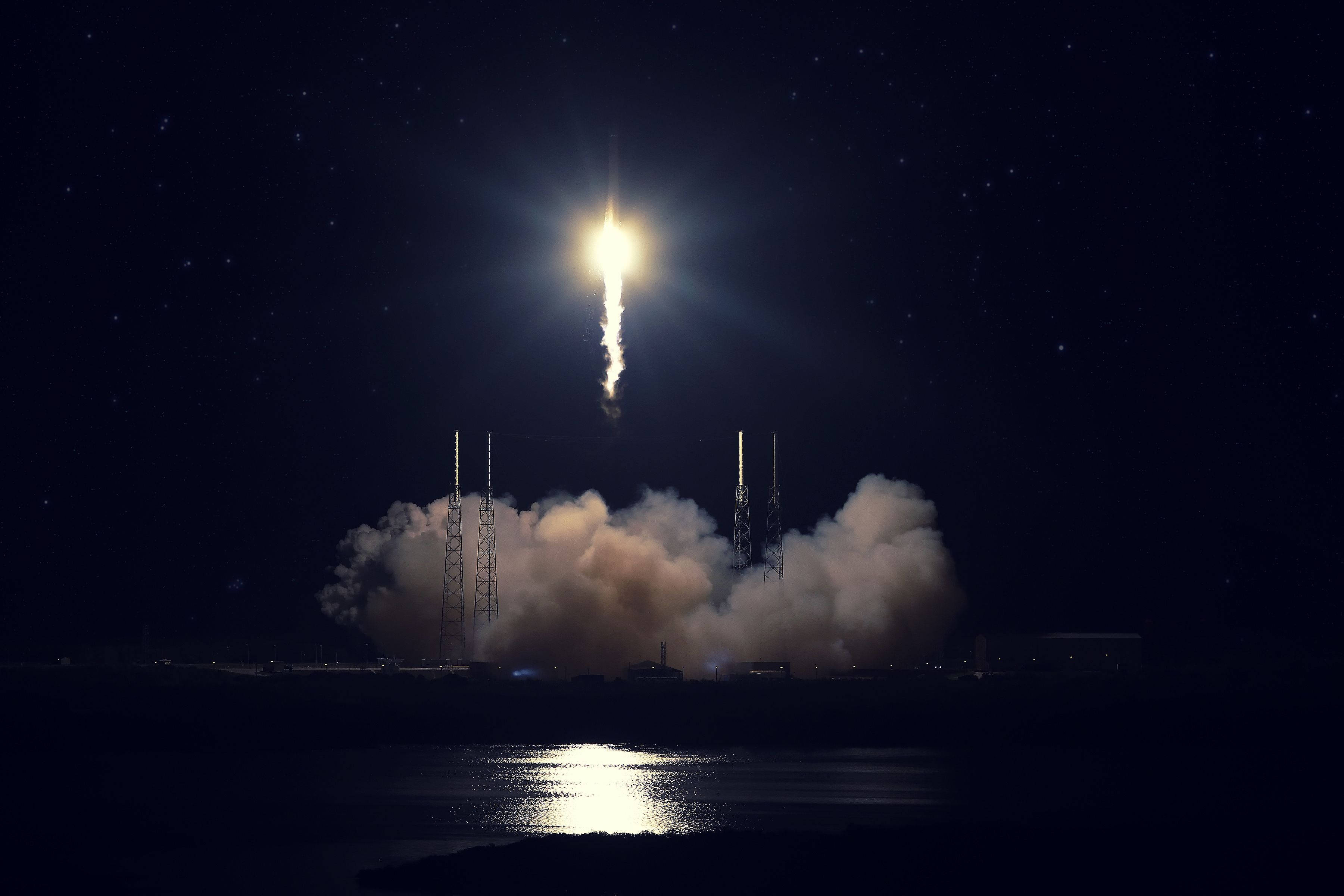 SpaceX 桌布 壁紙 — 火箭升入繁星點點的夜空，留下一道明亮軌跡，下方煙霧翻騰，倒映在水面上。