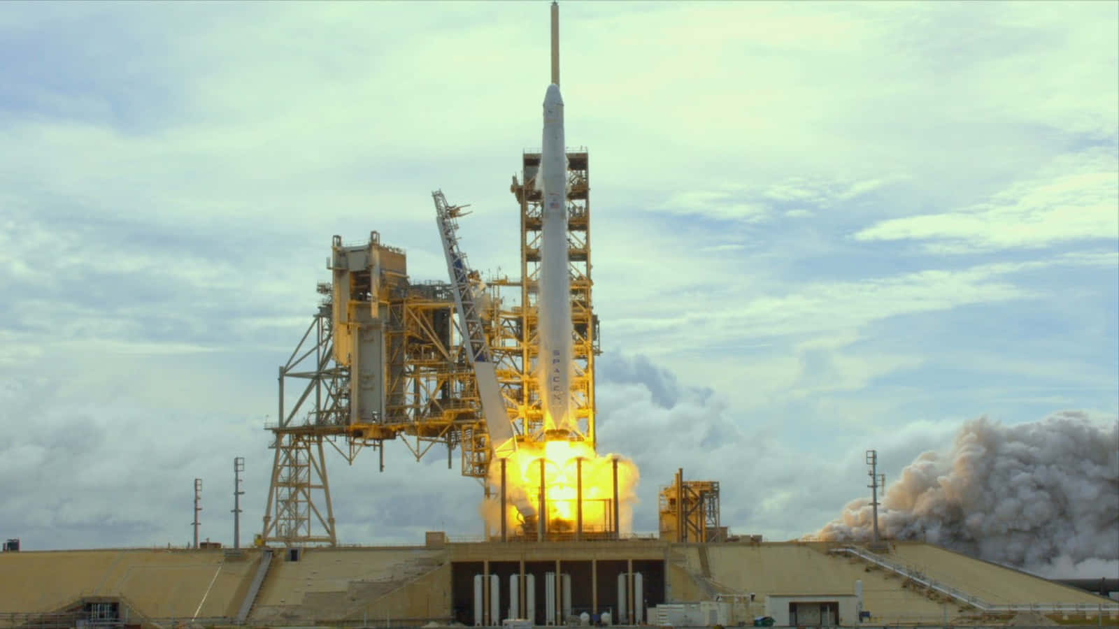 NASA 動態圖片 桌布 壁紙 — 火箭在發射台點燃，烈焰噴射，煙霧翻騰，天空多雲。