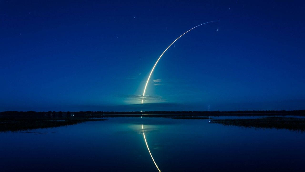 SpaceX 桌布 壁紙 — 火箭明亮的弧線劃過夜空，下方平靜的湖面反射出其發光的路徑。