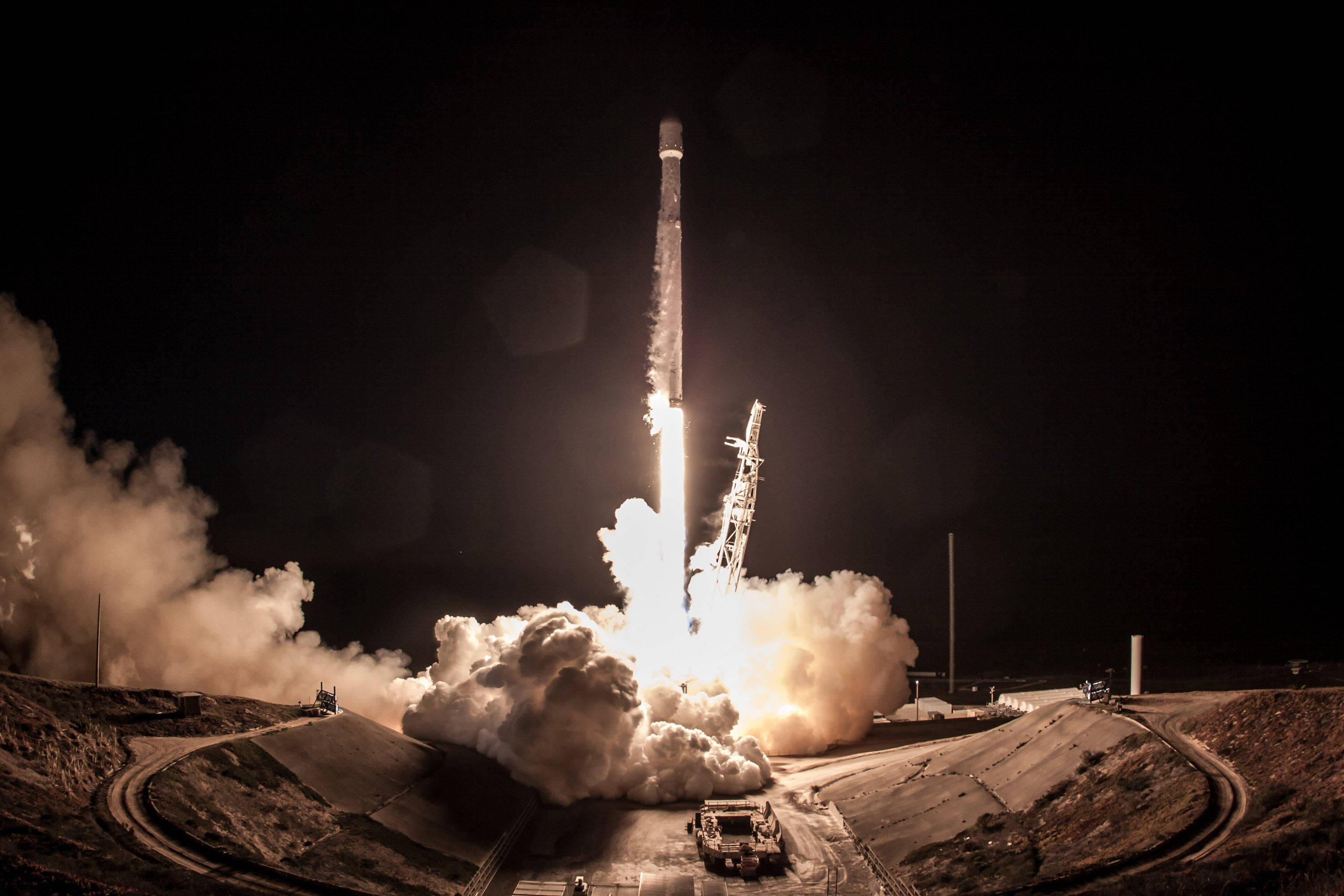 SpaceX 桌布 壁紙 — 火箭點火並升入夜空，在黑暗的沙漠景觀中留下熾熱的尾跡和滾滾濃煙。