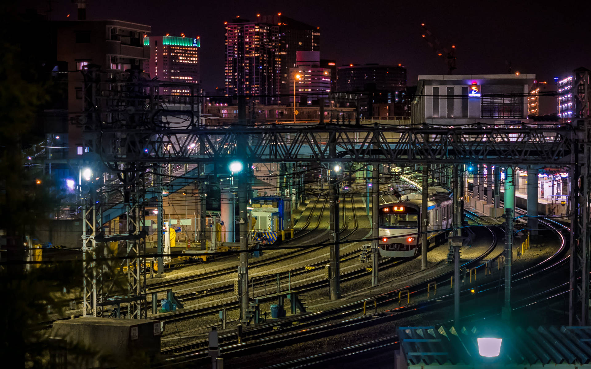 橫濱 桌布 壁紙 — 火車在夜間穿過霓虹燈閃爍的城市天際線下複雜的軌道網絡。