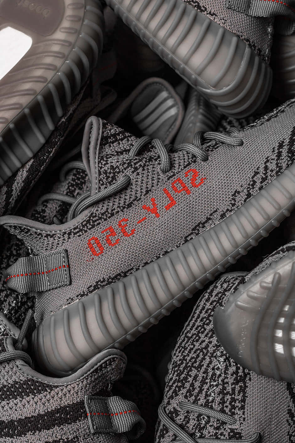 Yeezy 桌布 壁紙 — 灰色 Yeezy Boost 350 運動鞋堆疊在一起的特寫，鞋舌上可見紅色 'SPLY-350' 品牌標誌。