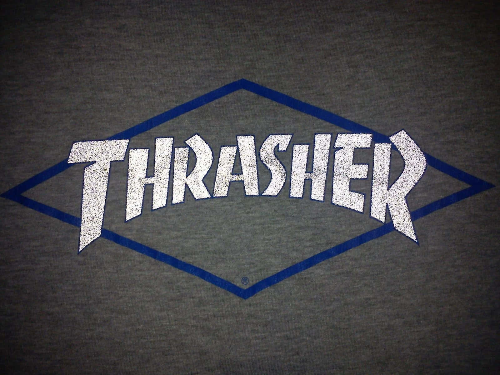 Thrasher 桌布 壁紙 — 灰色T恤的特寫，上面有一個磨損的白色Thrasher標誌，用藍色線條勾勒出菱形形狀。
