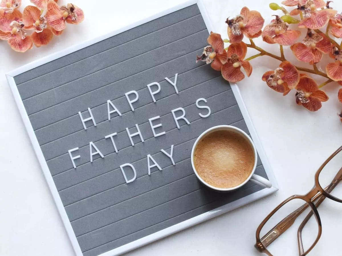 Fathers Day 桌布 壁紙 — 灰色字母板上顯示「HAPPY FATHERS DAY」，周圍環繞著粉紅色蘭花、一杯咖啡和眼鏡，放在白色表面上。