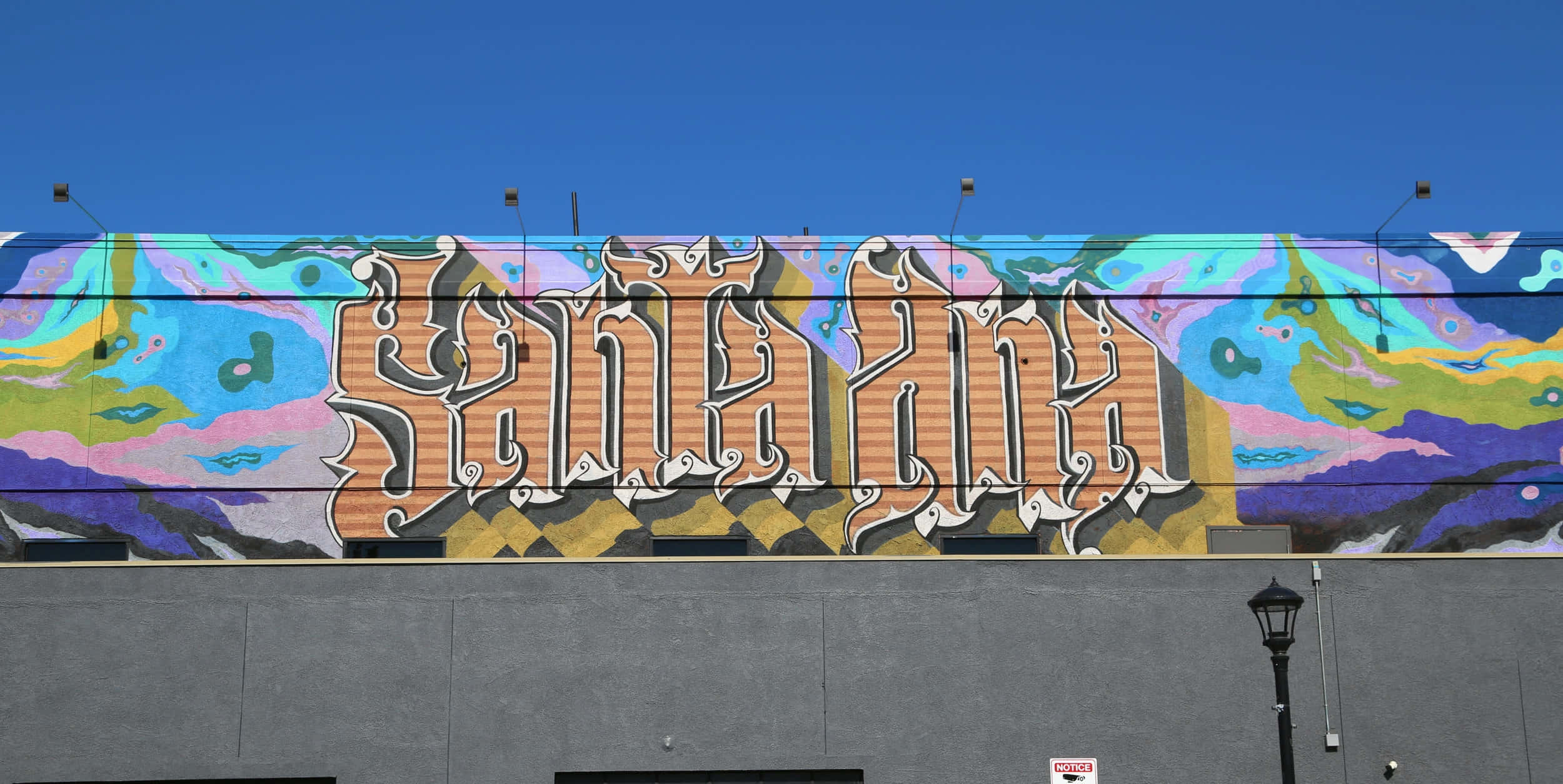Art Desktop 桌布 壁紙 — 灰色建築物外牆上，以華麗字體拼寫「SANTA ANA」的鮮豔塗鴉壁畫，背景是清澈的藍天。