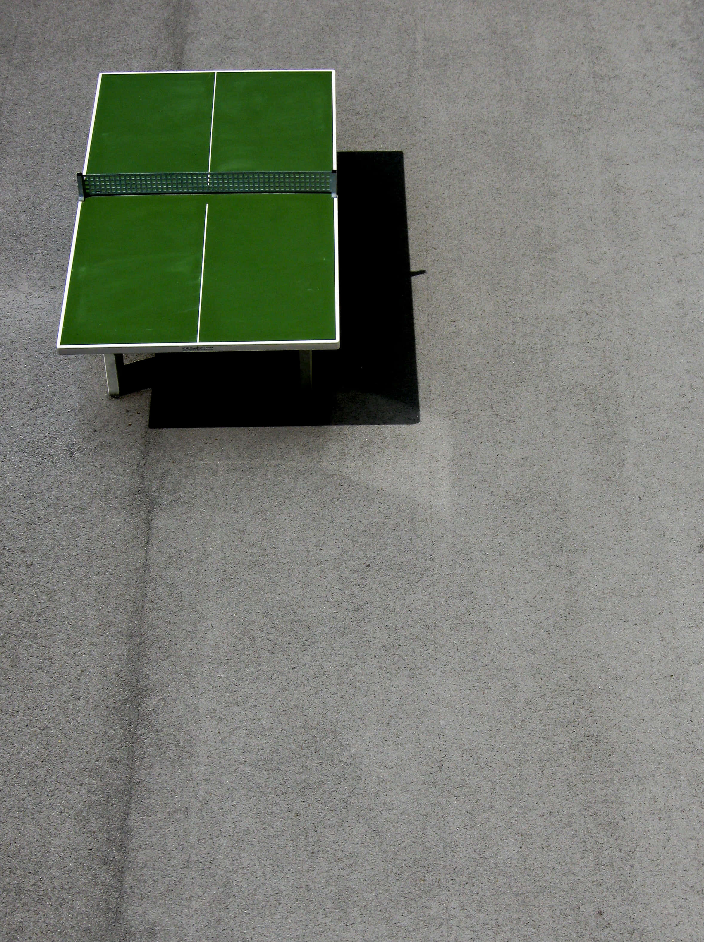 Table Tennis 桌布 壁紙 — 灰色混凝土上一個綠色乒乓球桌的俯視圖，黑色球網投射出清晰的陰影。