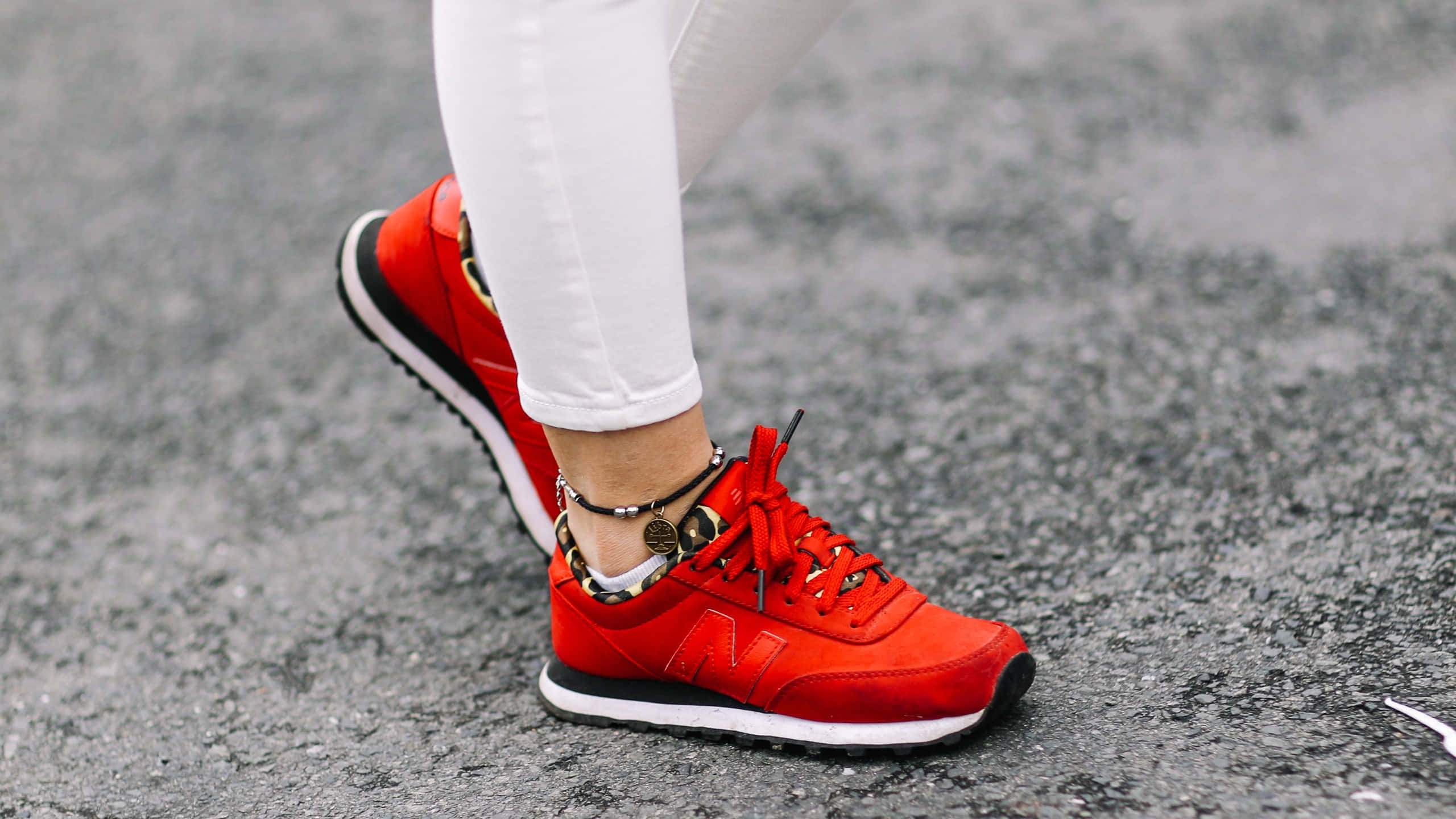 New Balance 桌布 壁紙 — 灰色瀝青表面上穿著白色褲子的鮮紅色運動鞋特寫。