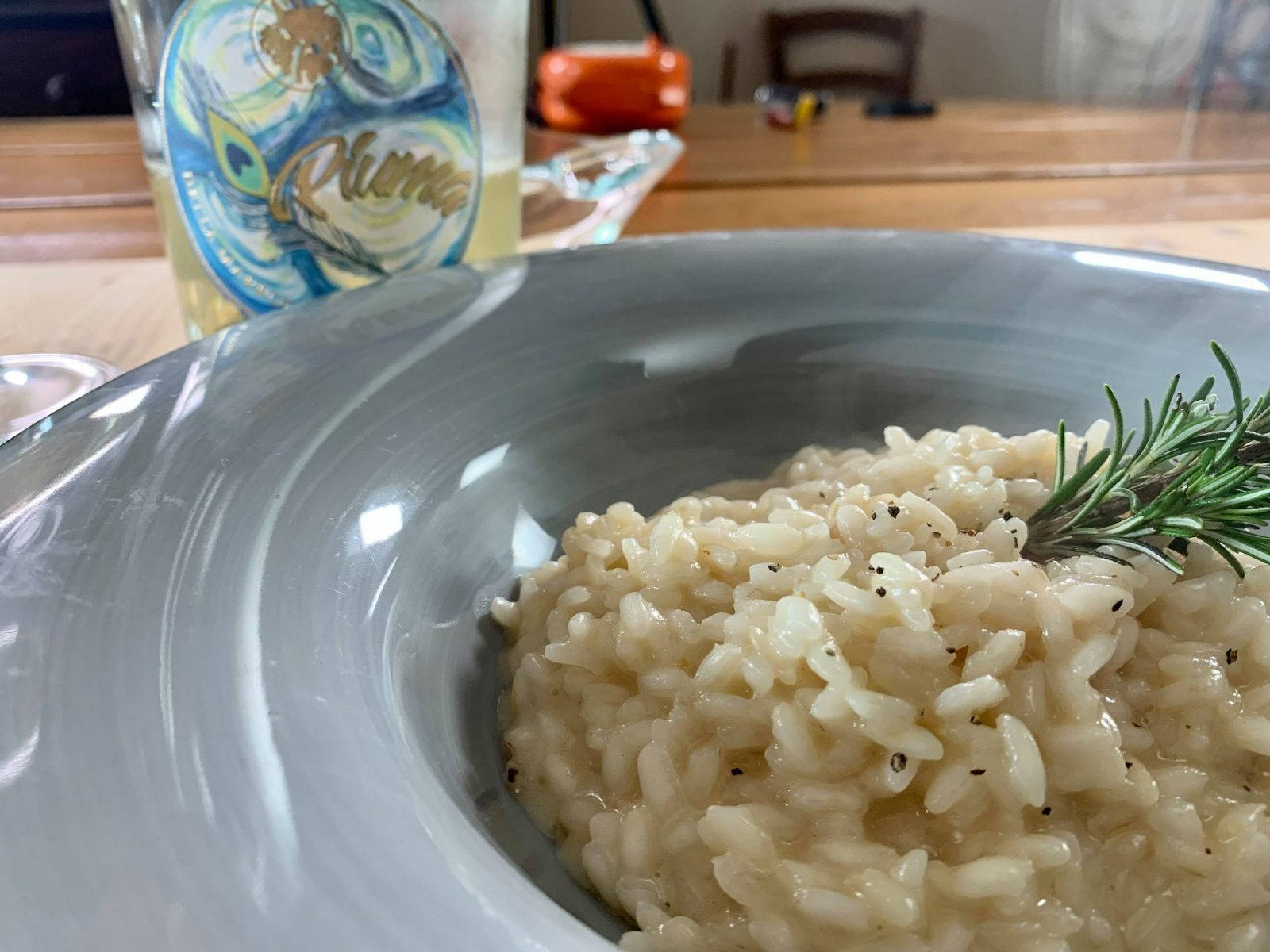 Rice 桌布 壁紙 — 灰色碗中奶油燴飯的特寫，飾以迷迭香和黑胡椒，背景有一瓶白葡萄酒。