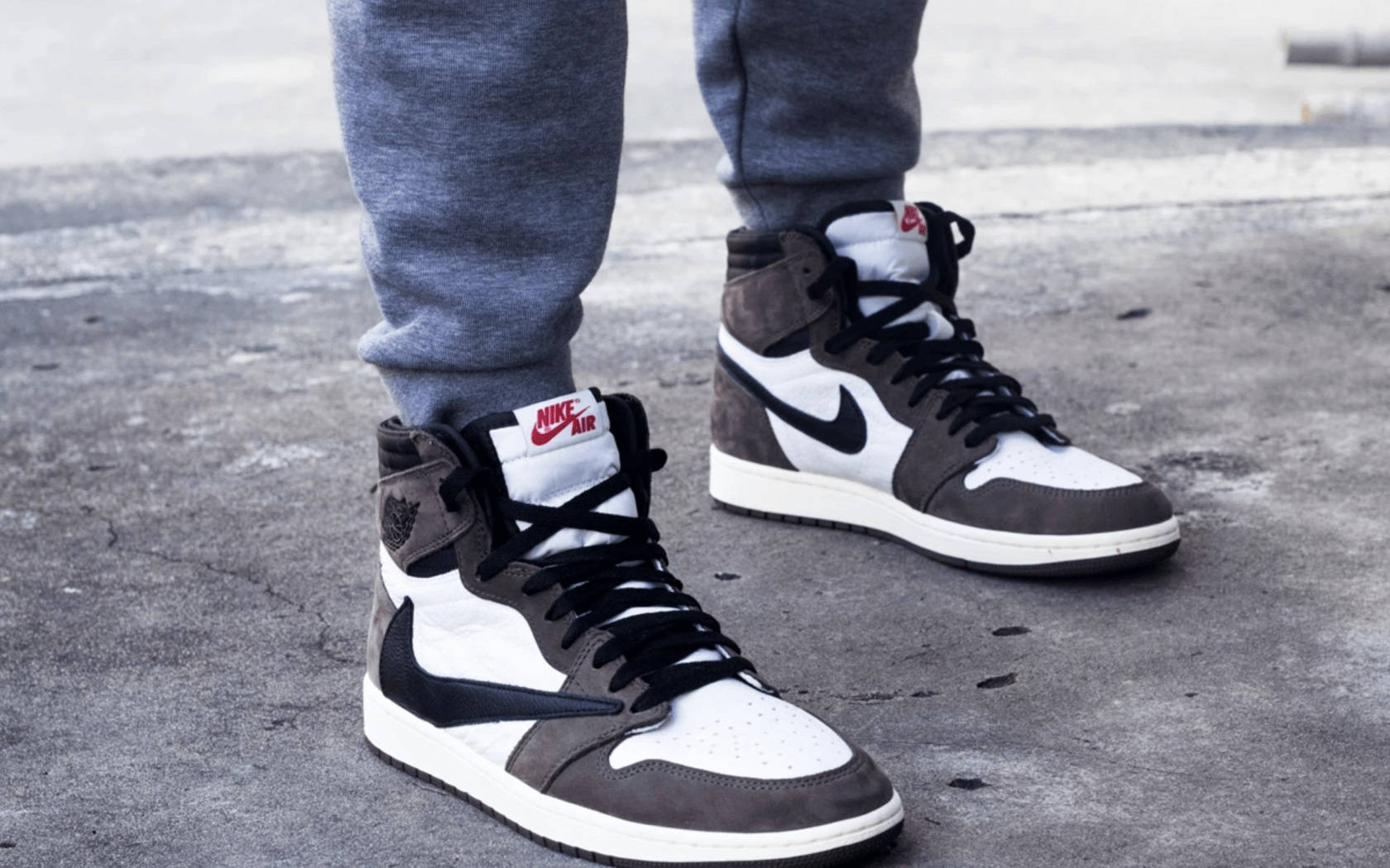 Travis Scott 桌布 壁紙 — 灰色運動褲和黑白灰色Nike Air Jordan運動鞋在裂開的混凝土路面上的特寫。