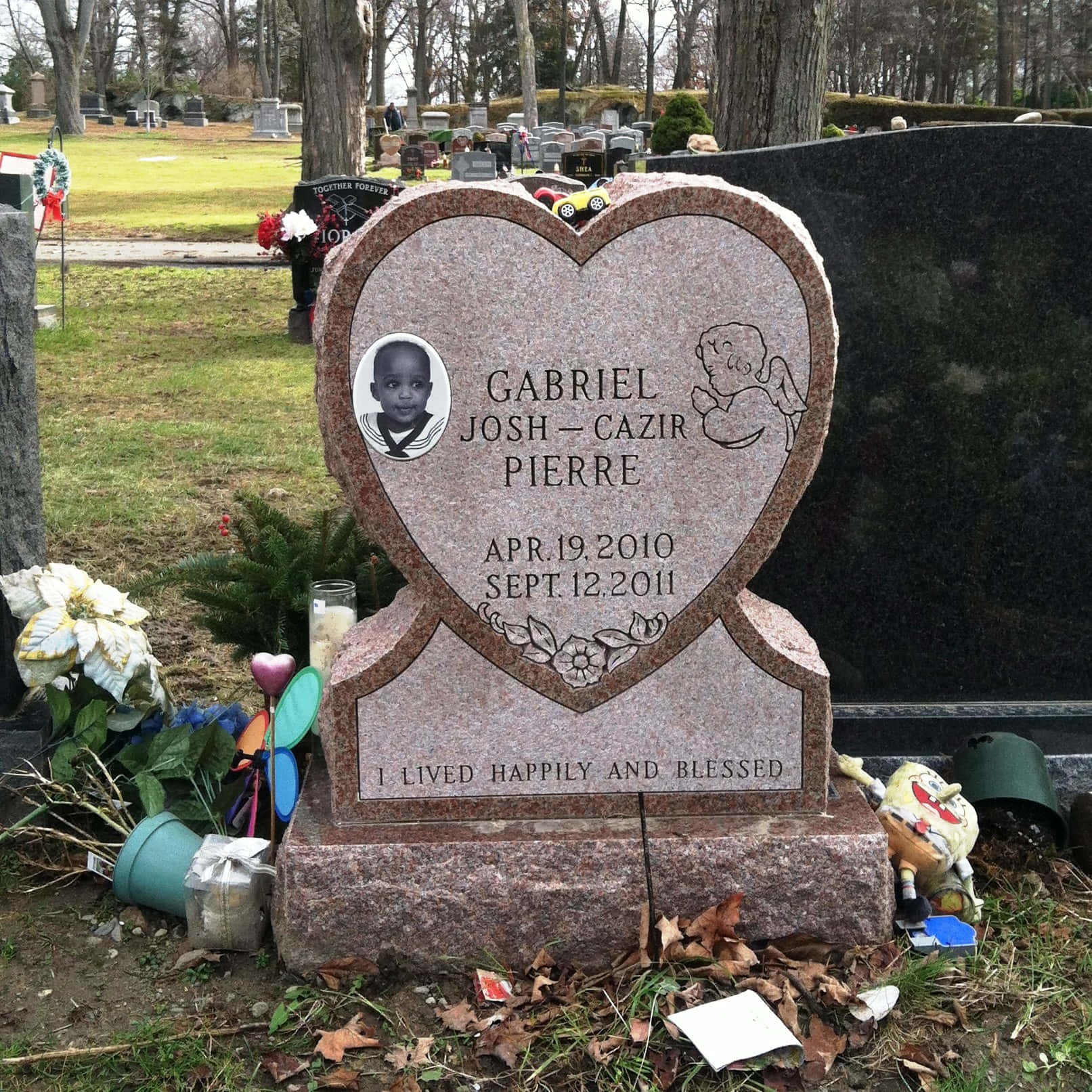 Memorial 桌布 壁紙 — 為Gabriel Josh-Cazir Pierre而設的心形花崗岩墓碑，飾有照片、天使雕刻和鮮花，周圍是墓園中的落葉。