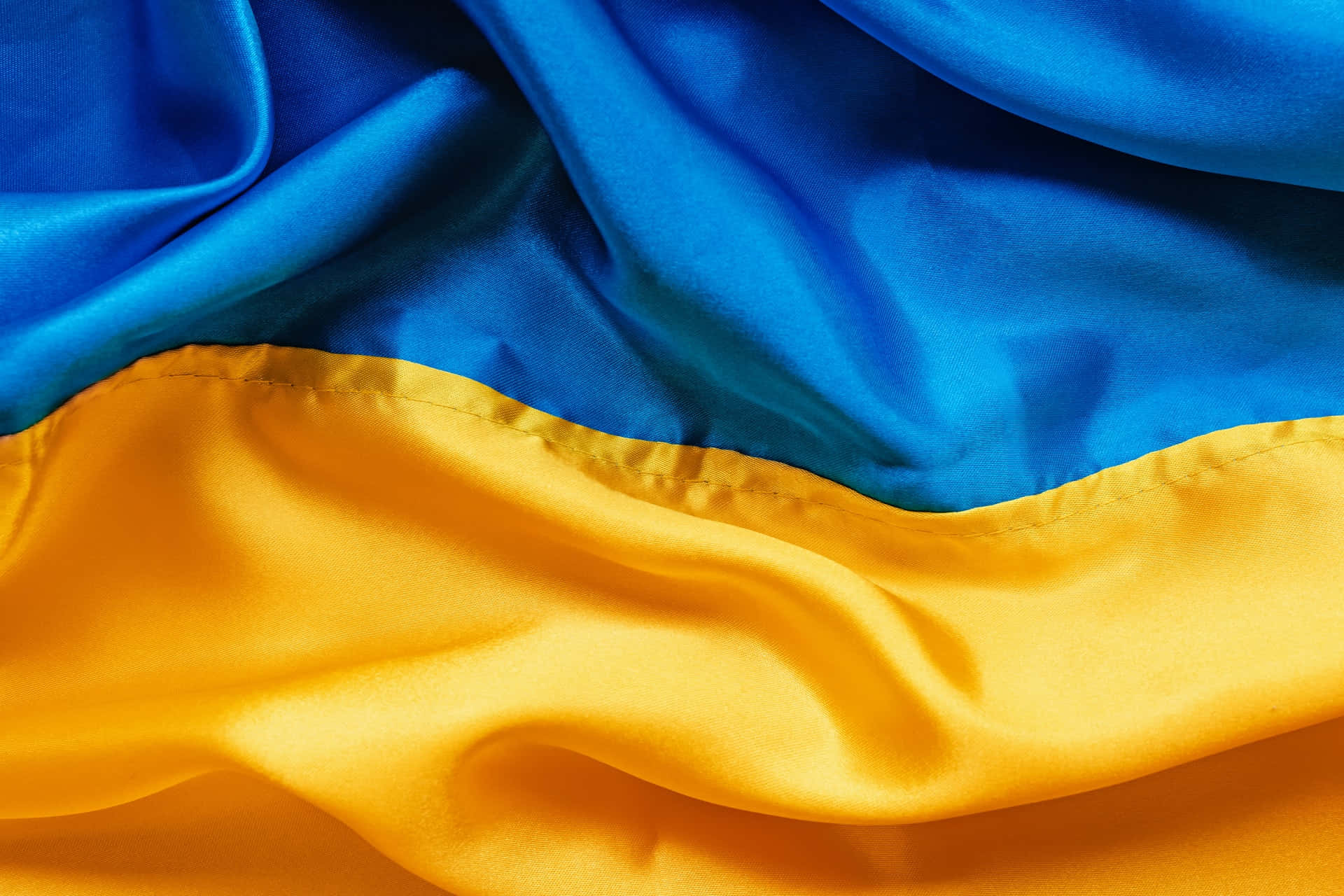 Ukraine 桌布 壁紙 — 烏克蘭國旗布料的特寫，鮮豔的藍色和黃色條紋在柔軟的褶皺中飄動。