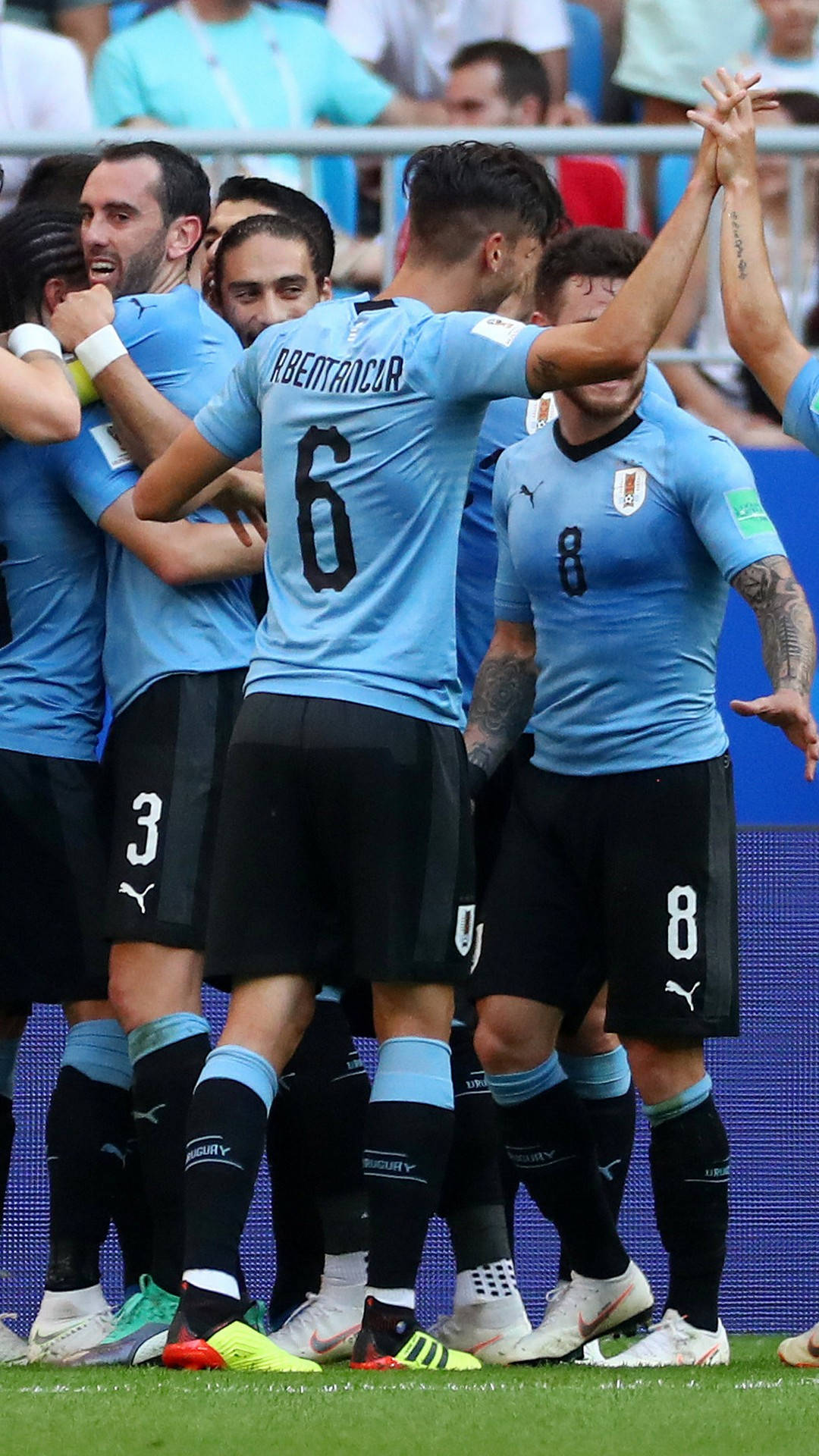 Uruguay 桌布 壁紙 — 烏拉圭足球員身穿淺藍色球衣，在充滿活力的綠色球場上高舉雙臂、歡樂擁抱慶祝進球。