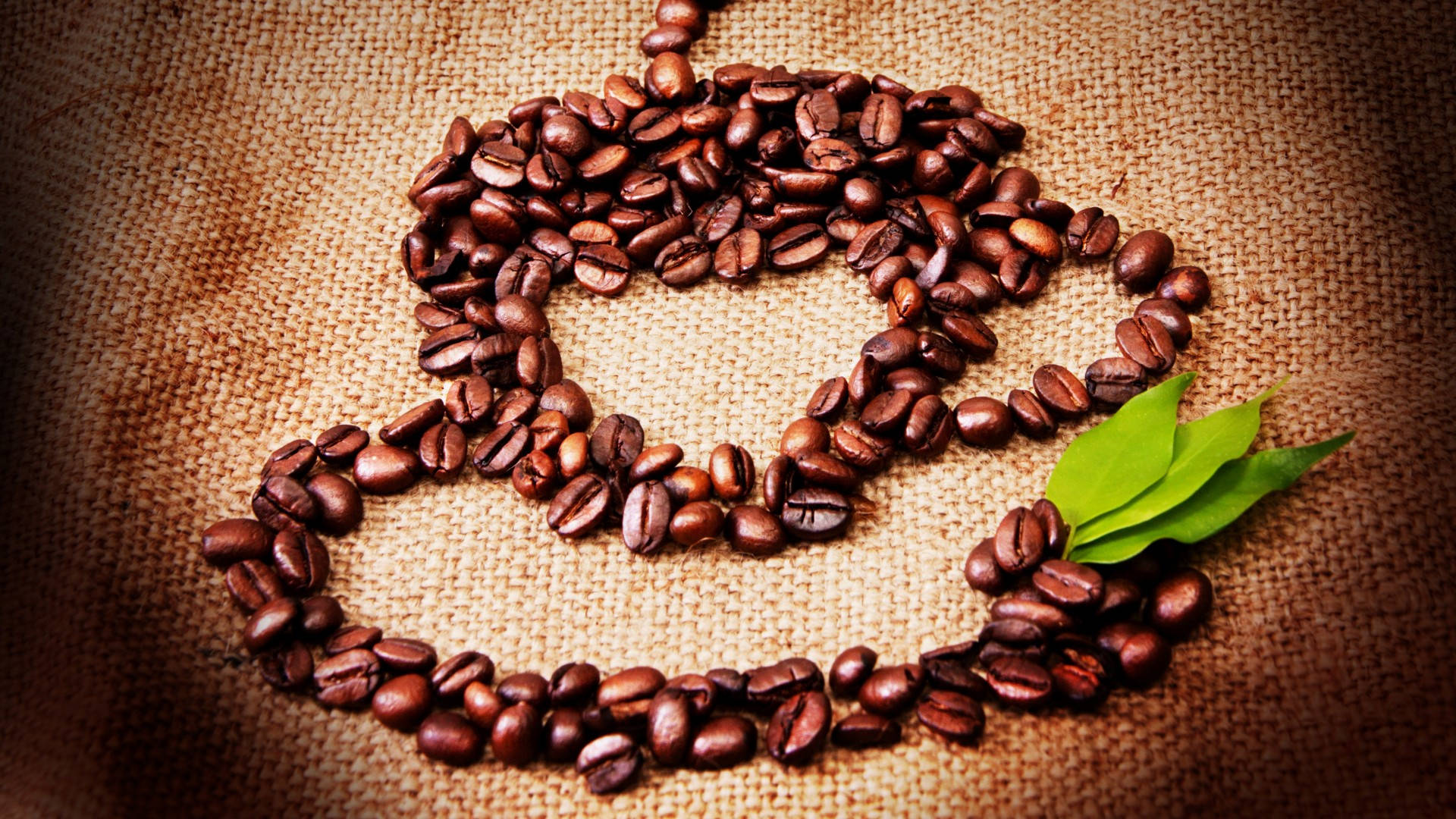 beans 桌布 壁紙 — 烘焙咖啡豆排列成杯形放在粗麻布上，旁邊有一片新鮮綠葉。